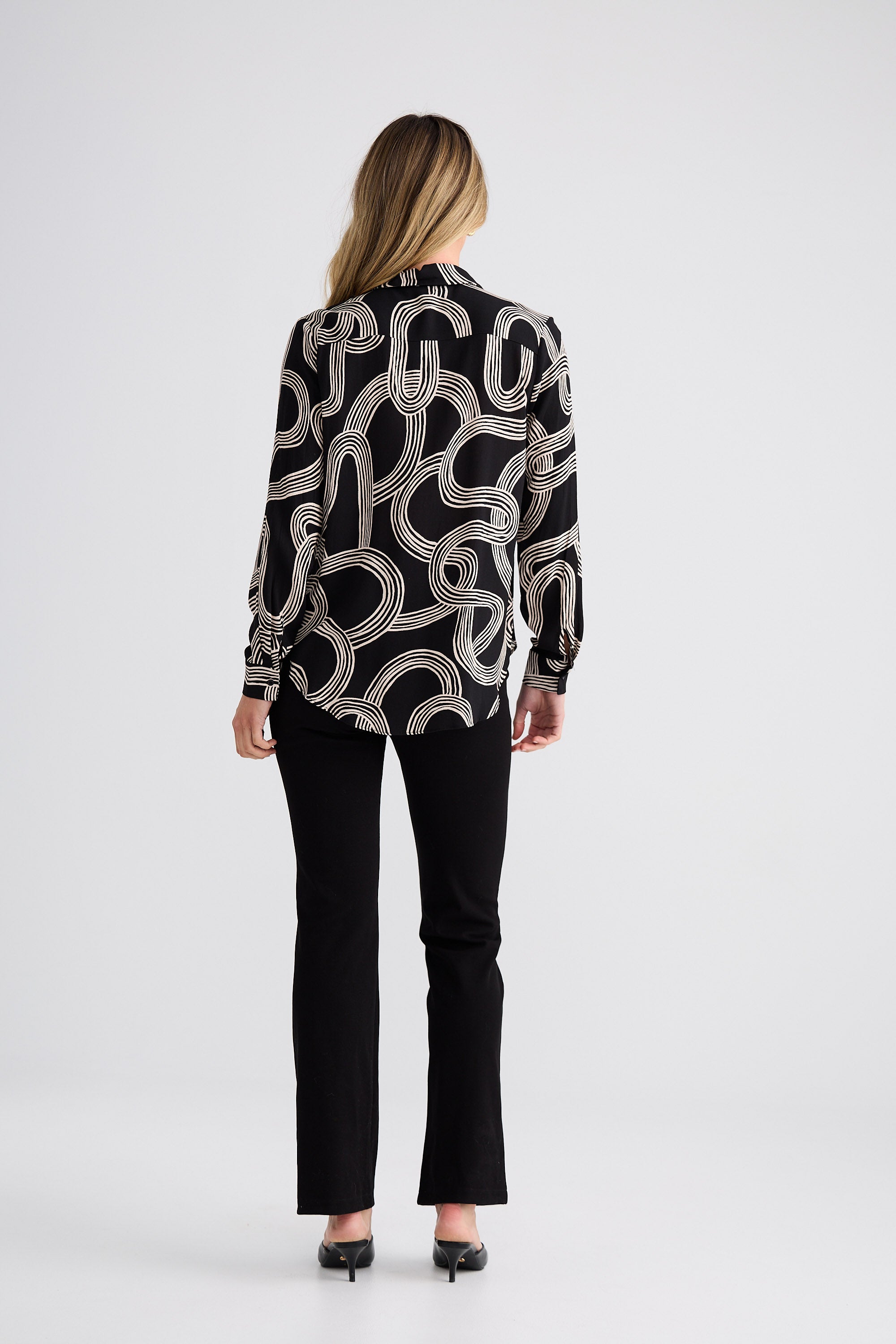 Woman wearing a black and white patterned blouse with black pants on a white background