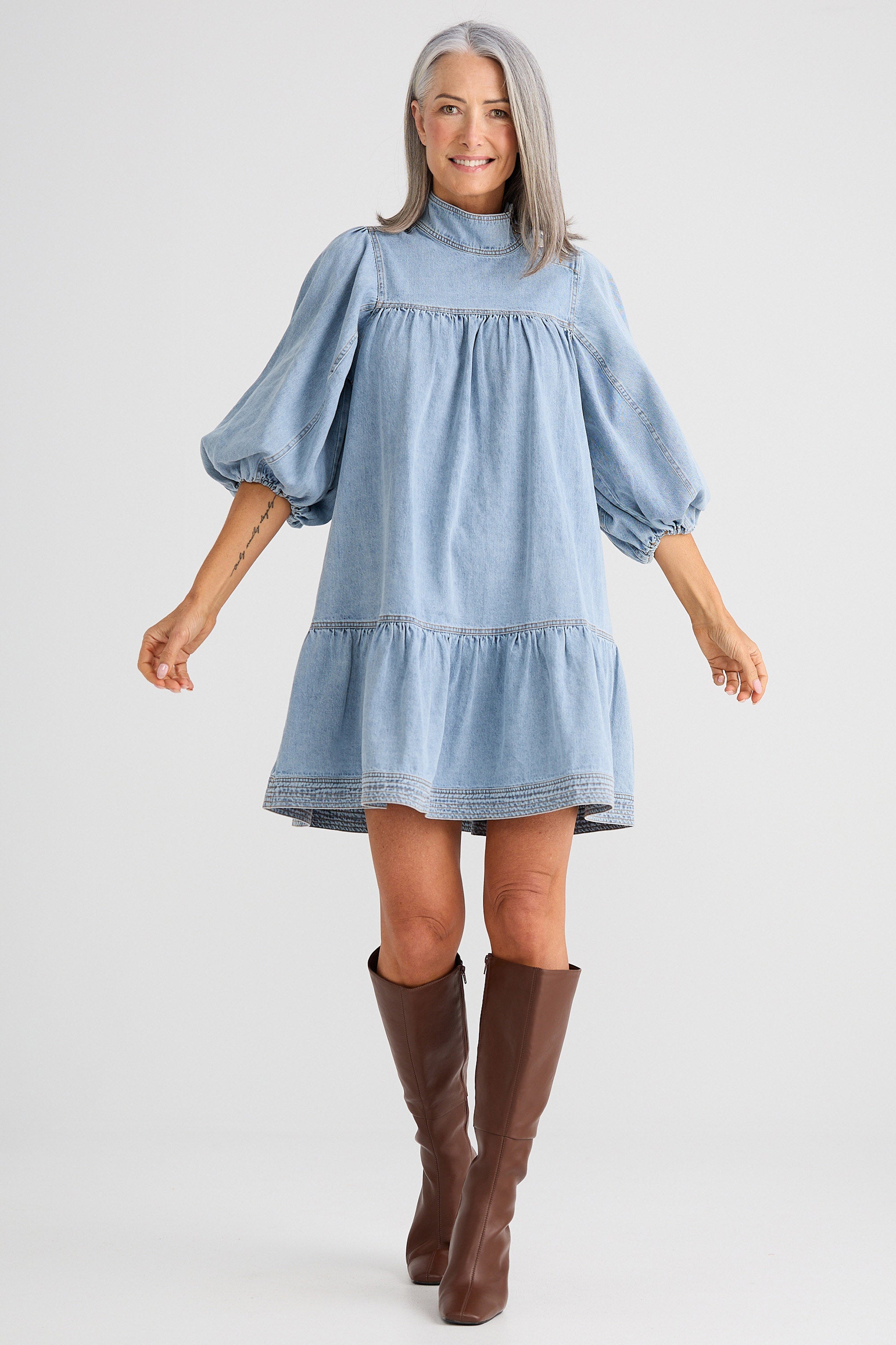 Woman wearing a light blue dress with puffed sleeves and brown knee-high boots on a white background