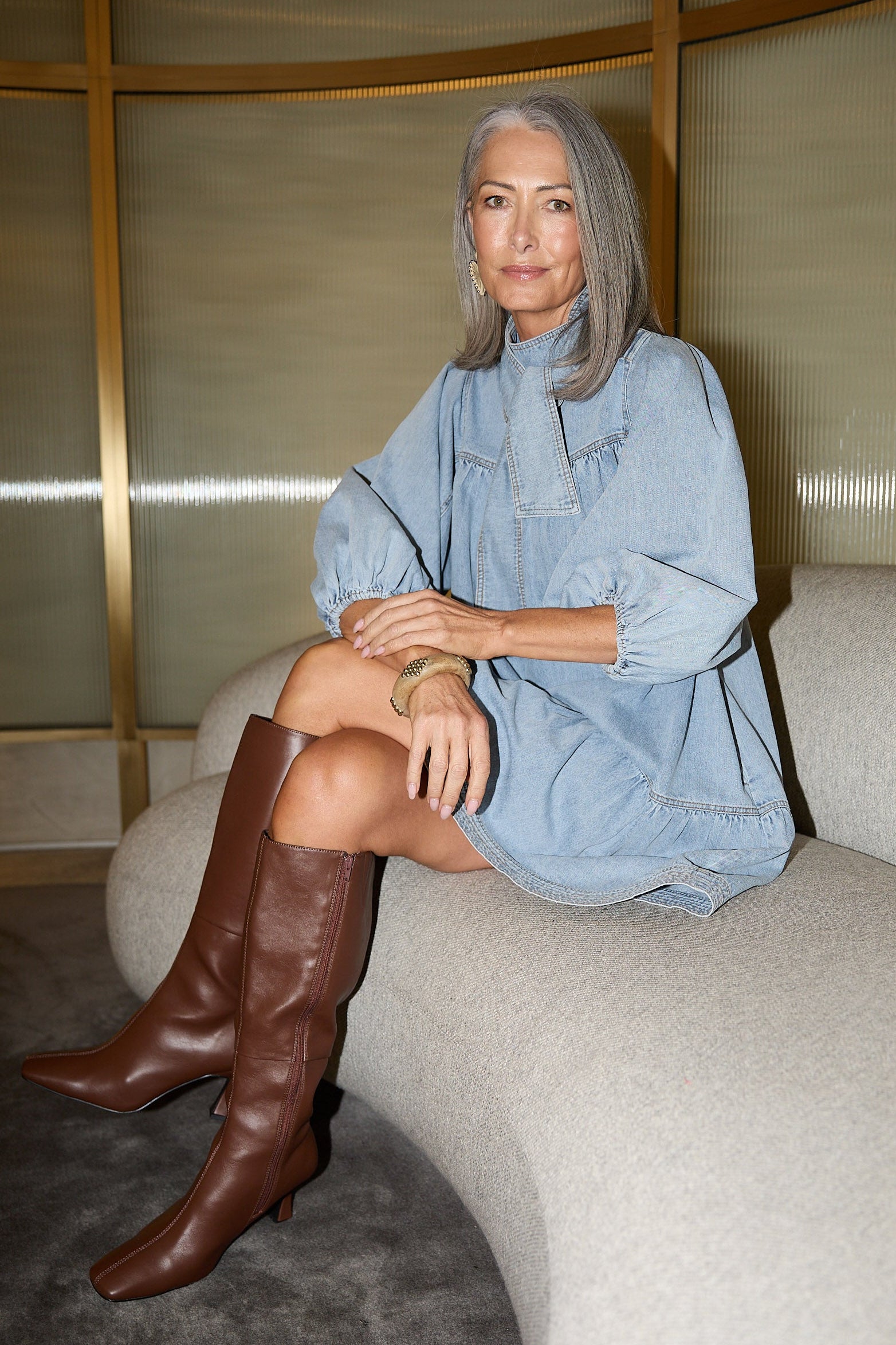 Woman in a blue dress and brown knee-high boots sitting on a white couch.