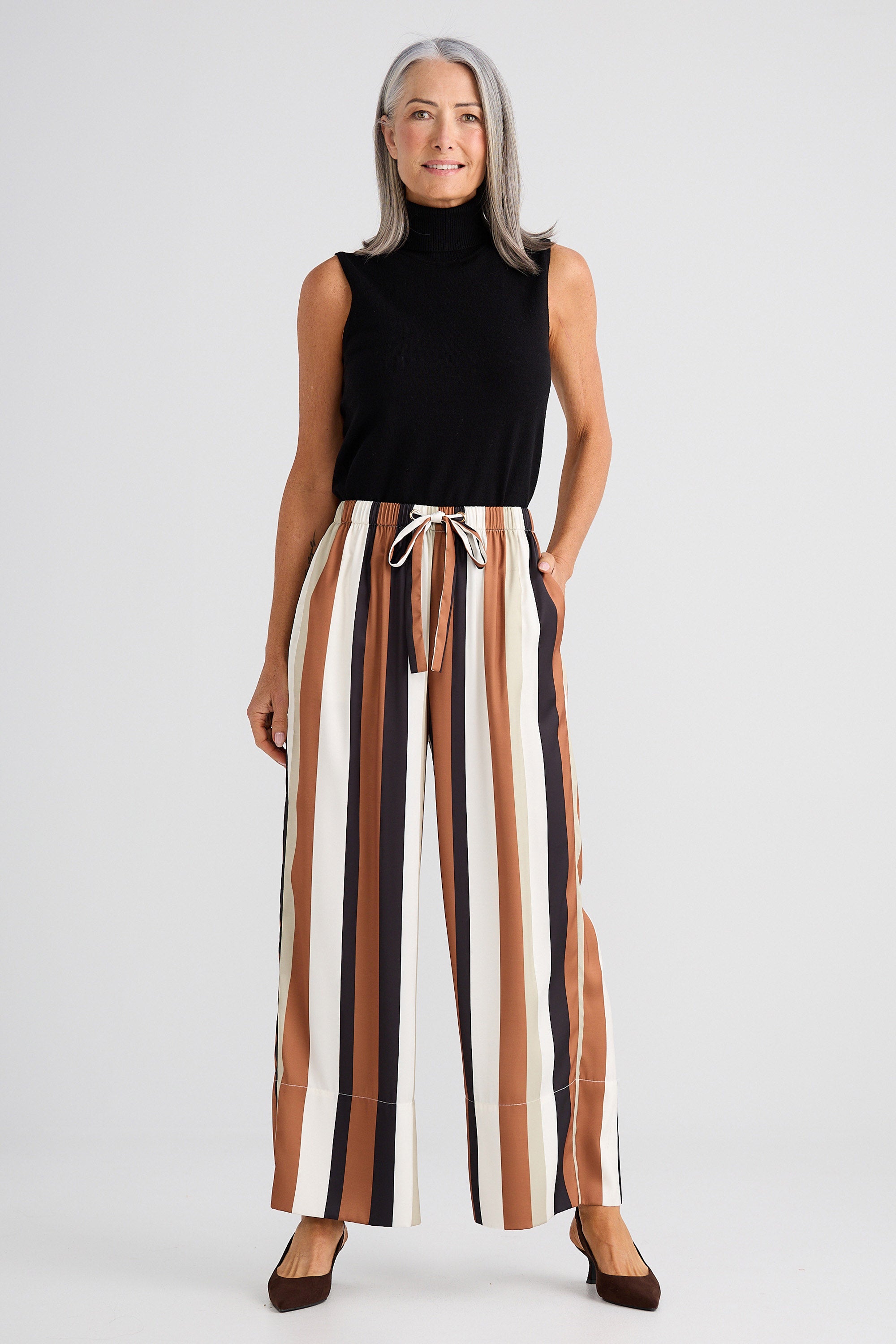 Woman wearing a black sleeveless top and striped pants on a white background