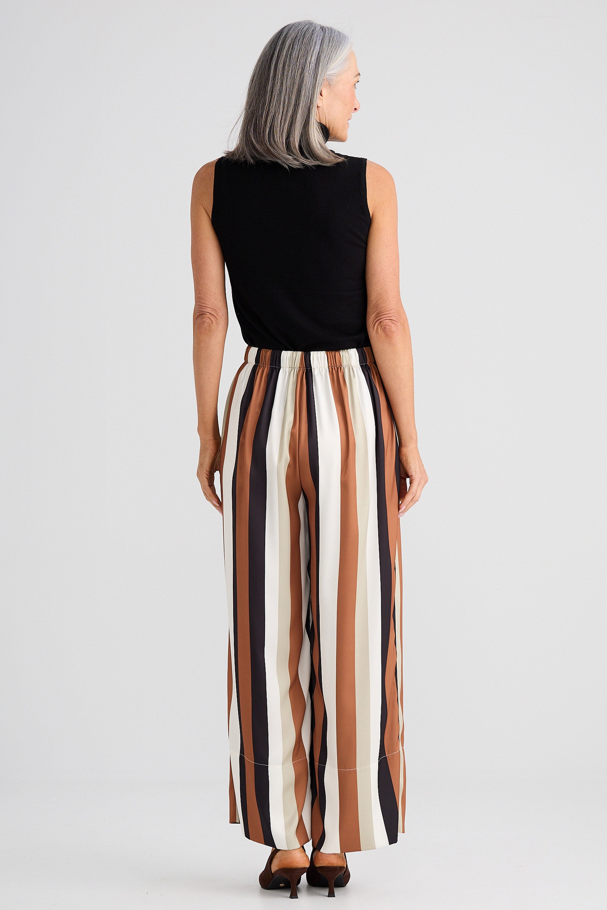 Woman wearing a black sleeveless top and striped pants on a light gray background