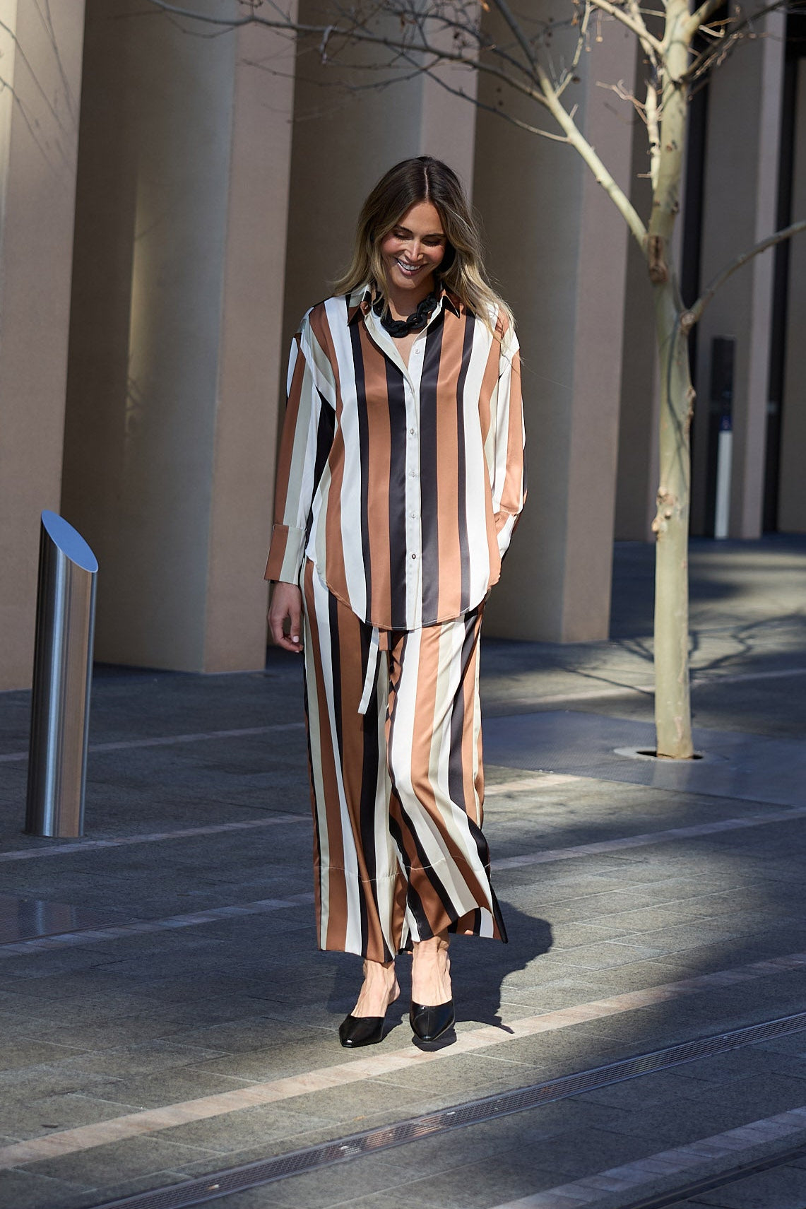 Woman in a striped outfit standing in front of a modern building with bare trees.