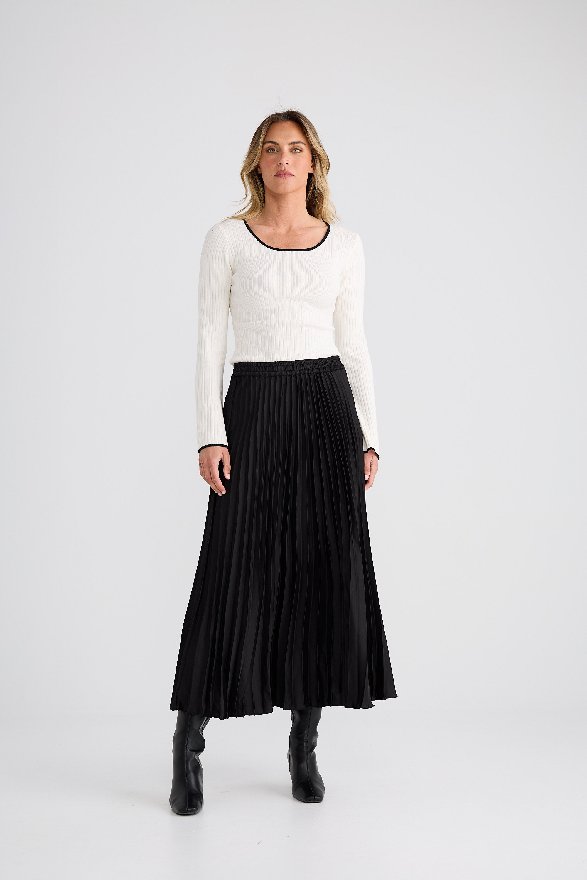 Woman wearing a white long-sleeve top and black pleated skirt on a white background
