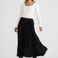 Woman wearing a white sweater and black pleated skirt on a white background