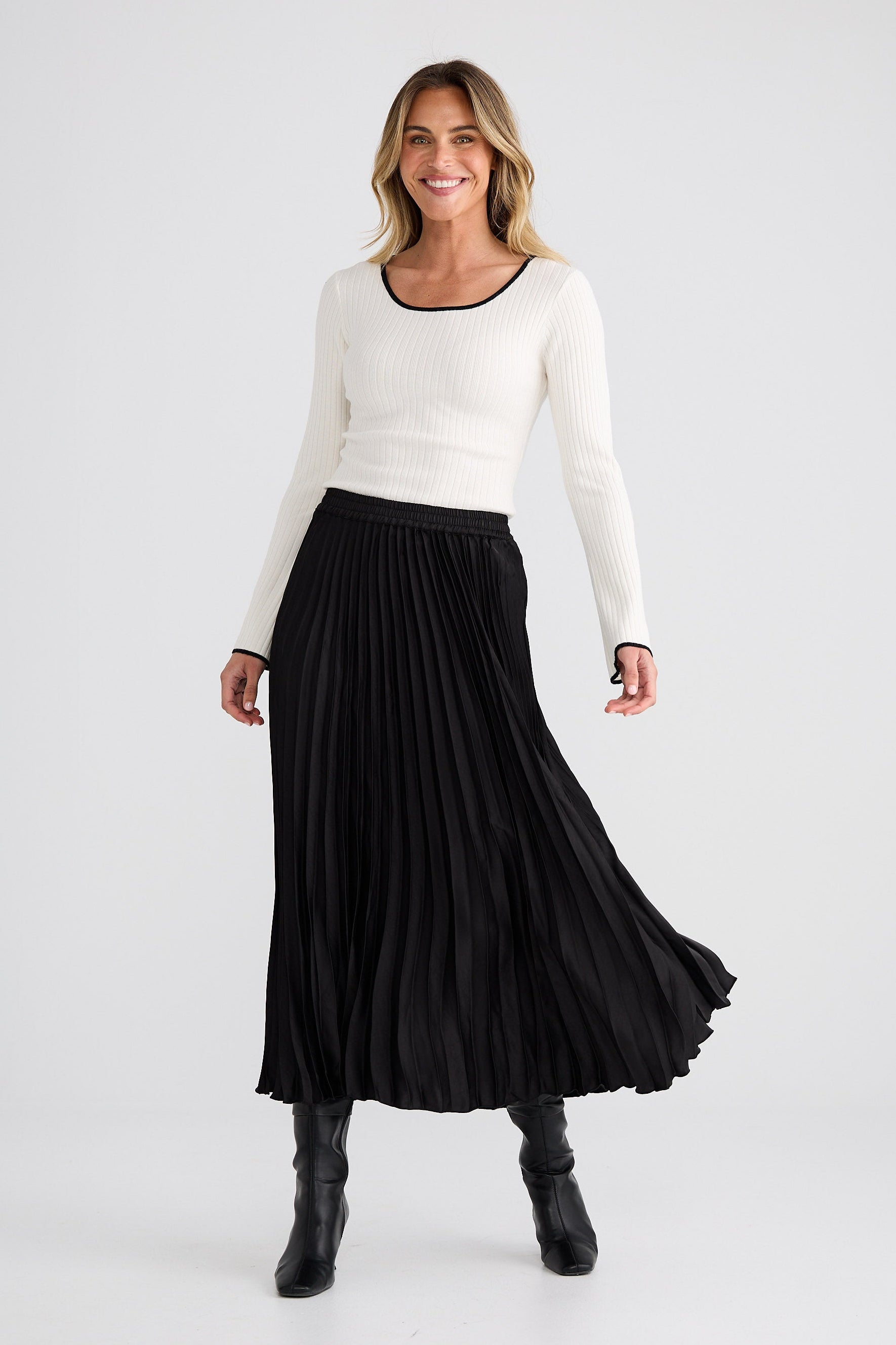 Woman wearing a white sweater and black pleated skirt on a white background