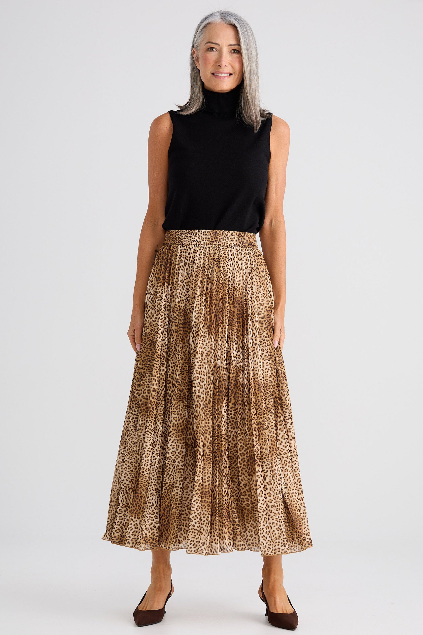 Woman wearing a black sleeveless top and gold patterned skirt on a white background