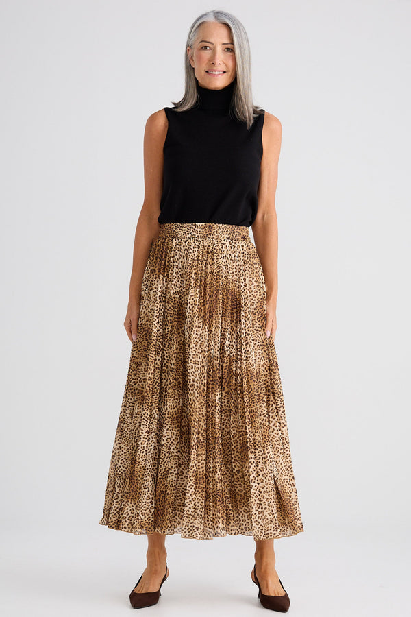 Woman wearing a black sleeveless top and gold patterned skirt on a white background