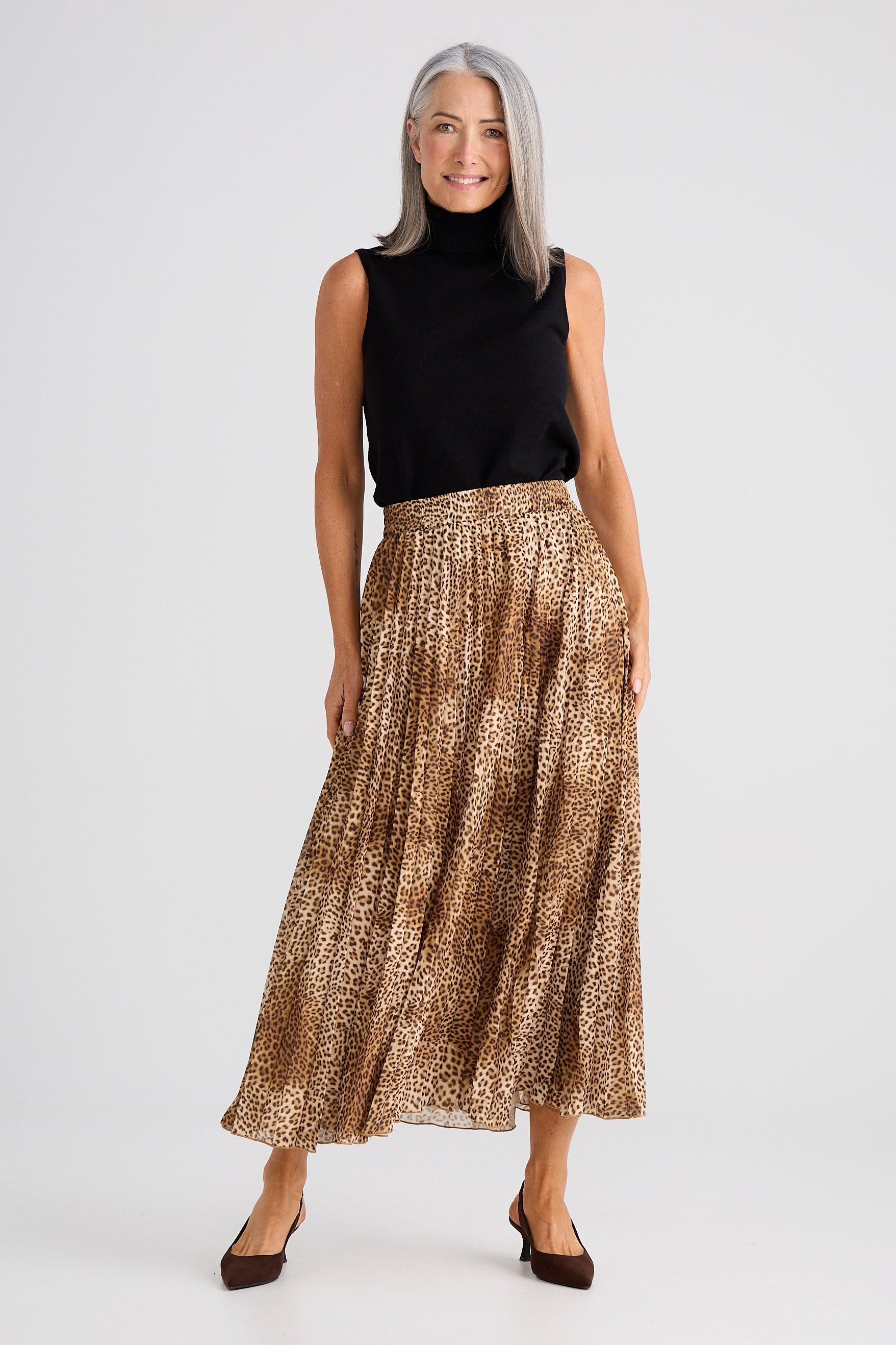 Woman wearing a black sleeveless top and gold patterned skirt on a white background