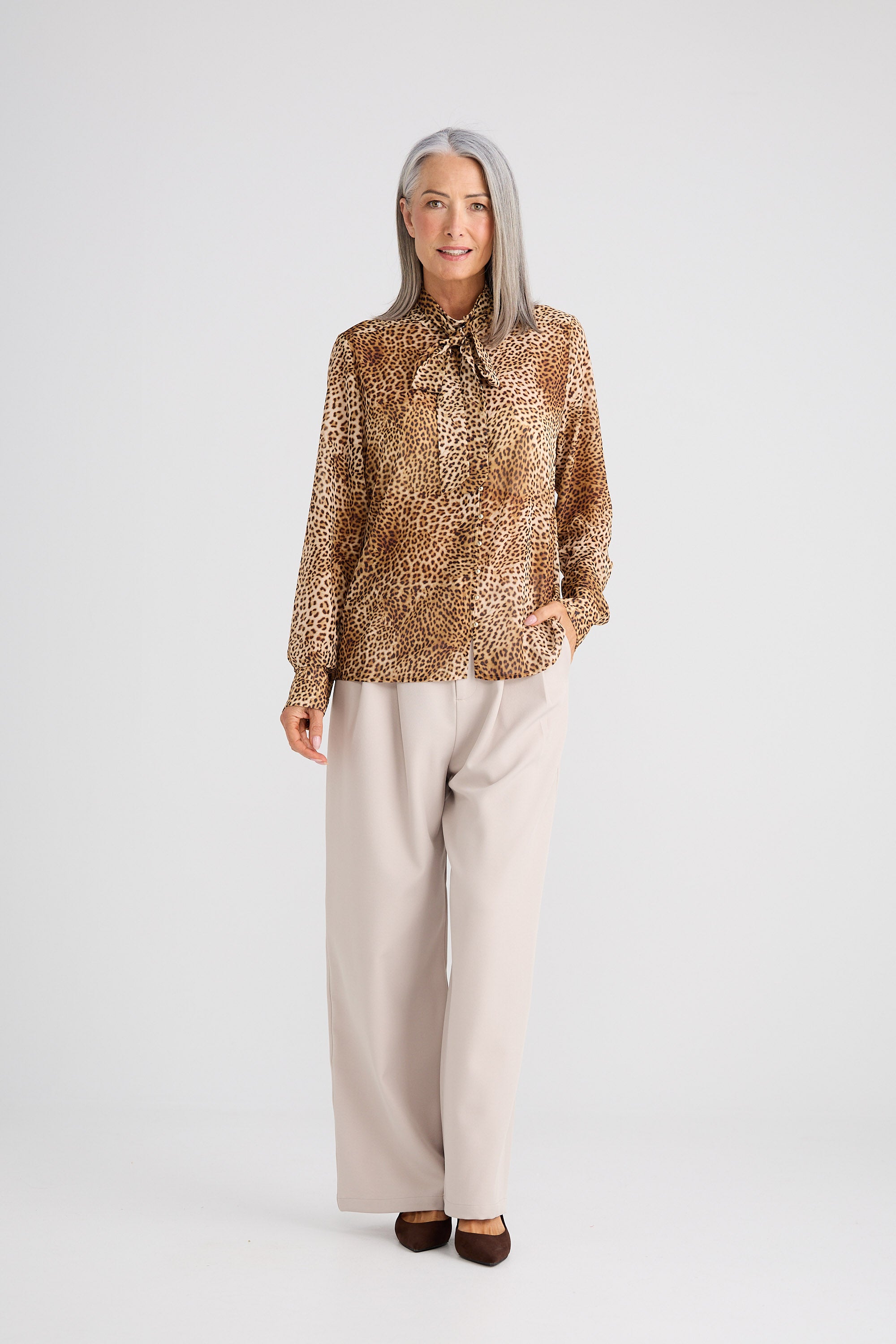 Woman wearing a patterned blouse and beige pants on a white background