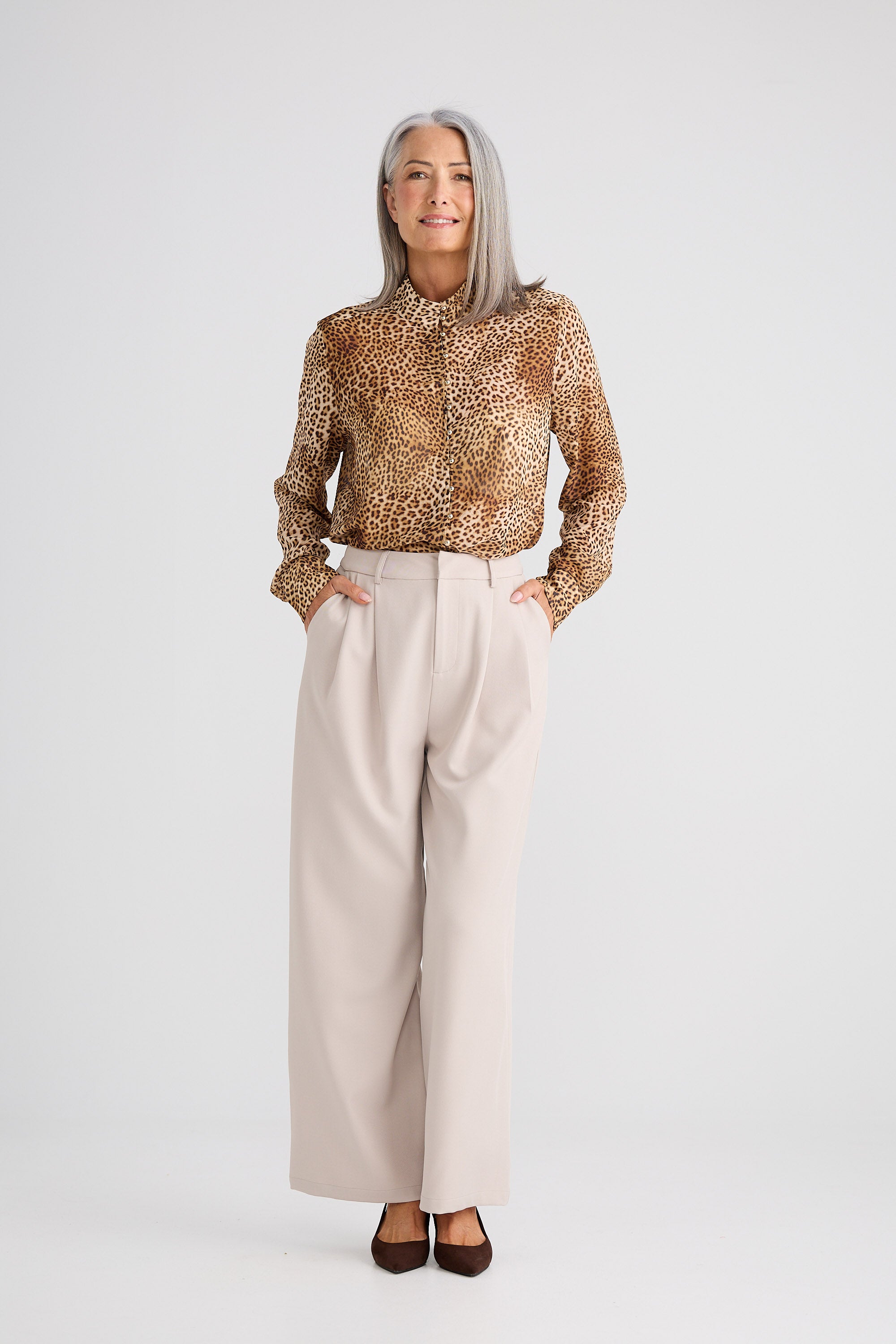 Woman wearing a patterned blouse and beige pants on a white background