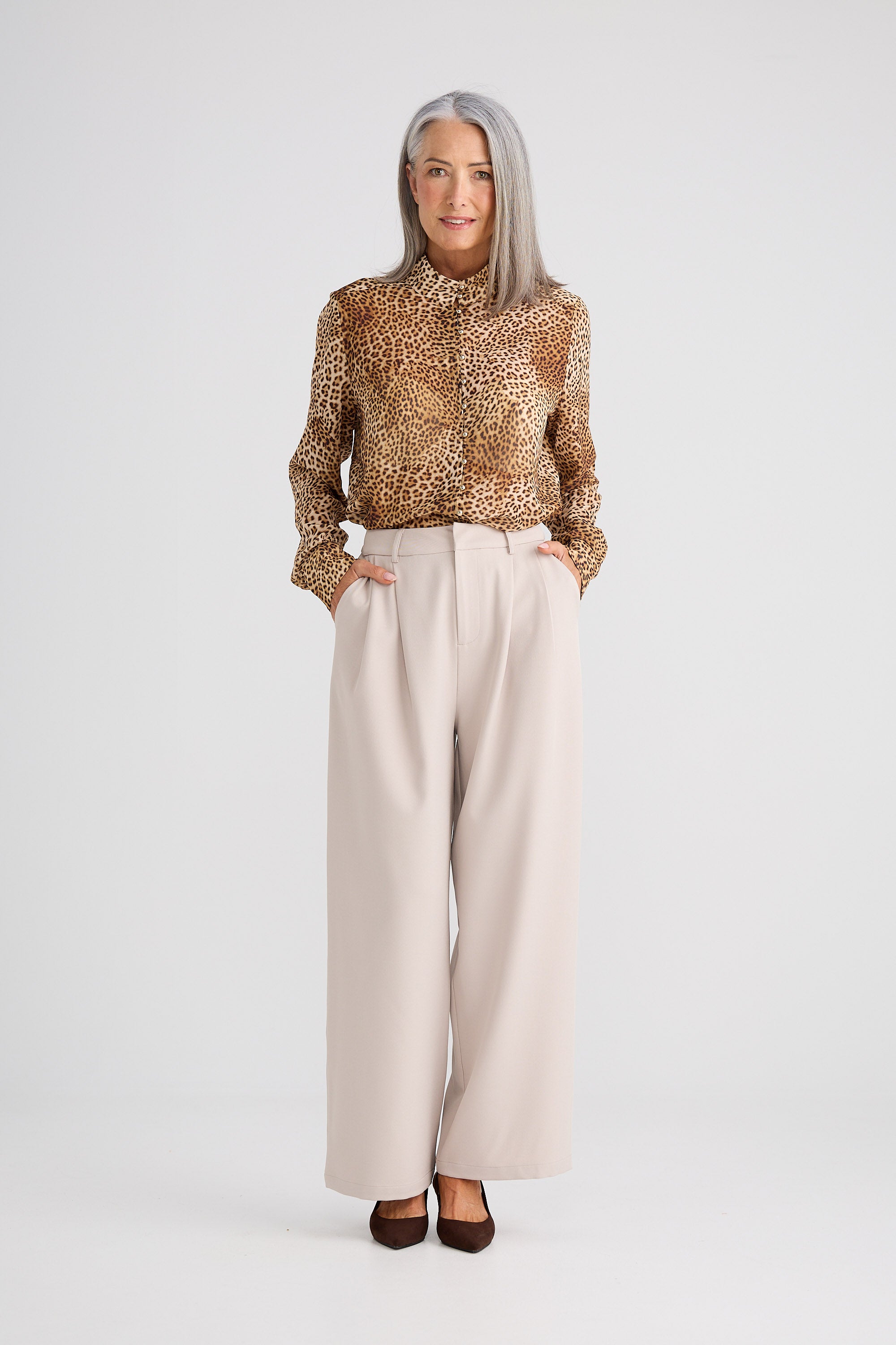 Woman wearing a patterned blouse and beige pants on a white background