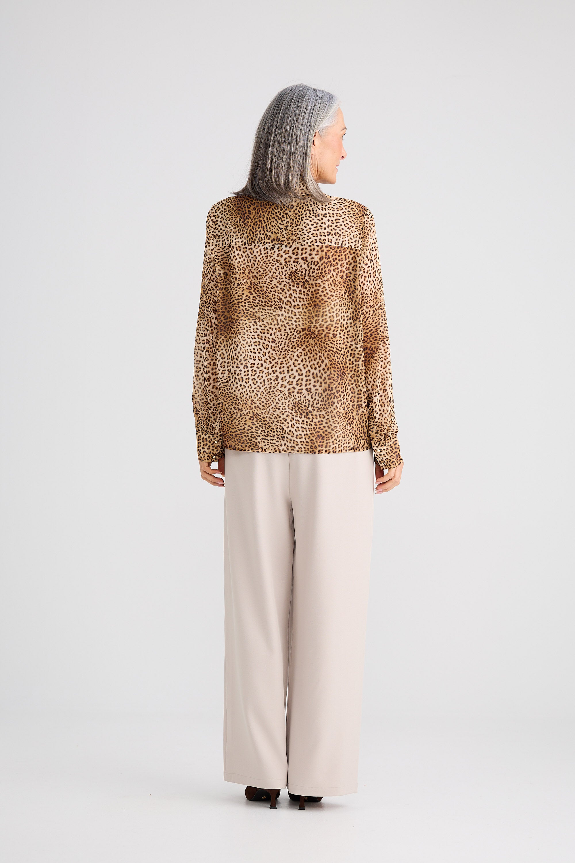 Person wearing a leopard print blouse and beige pants on a white background