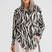 Woman wearing a black and white patterned blouse with beige pants on a light gray background