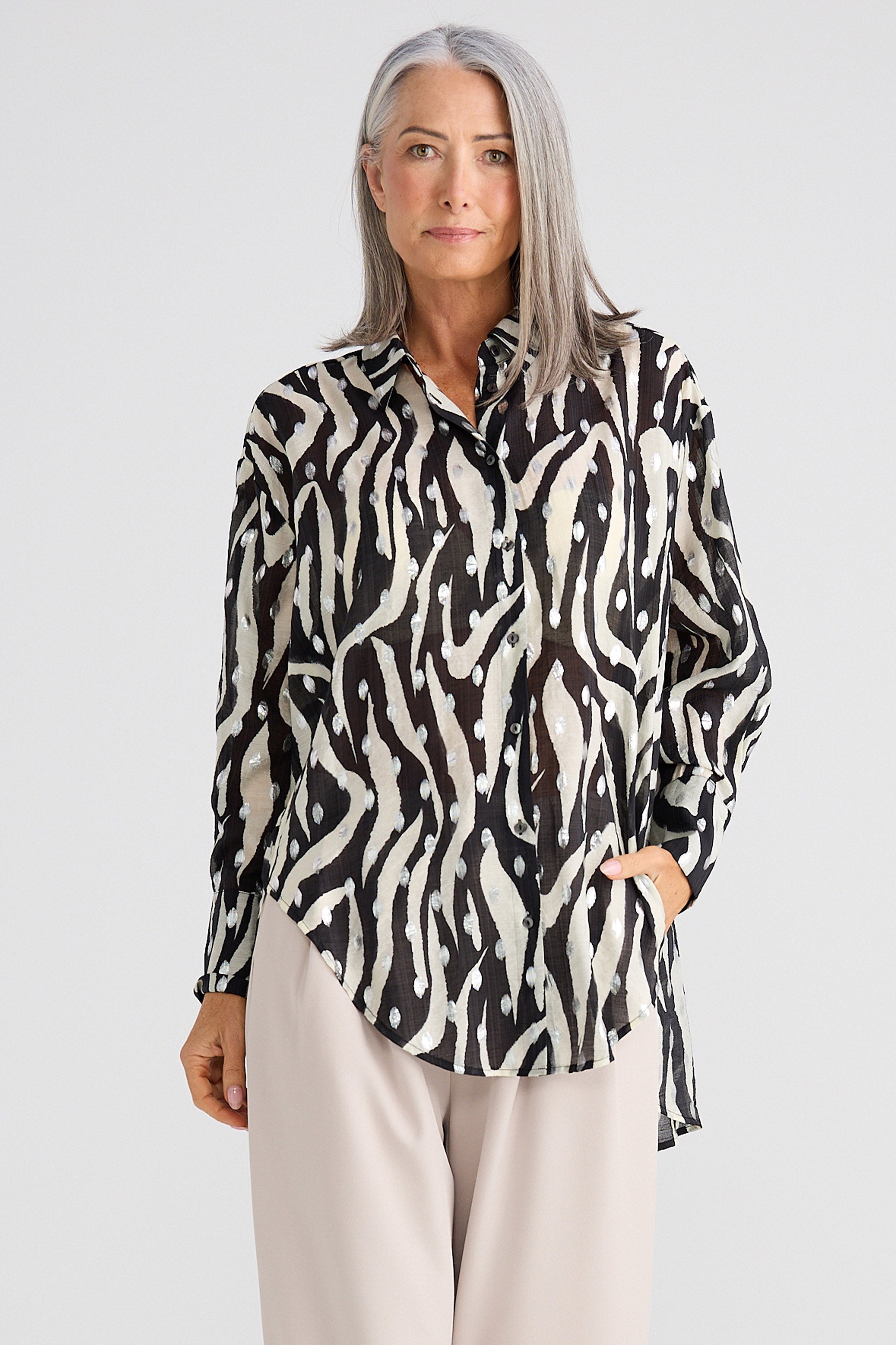 Woman wearing a black and white patterned blouse with beige pants on a light gray background