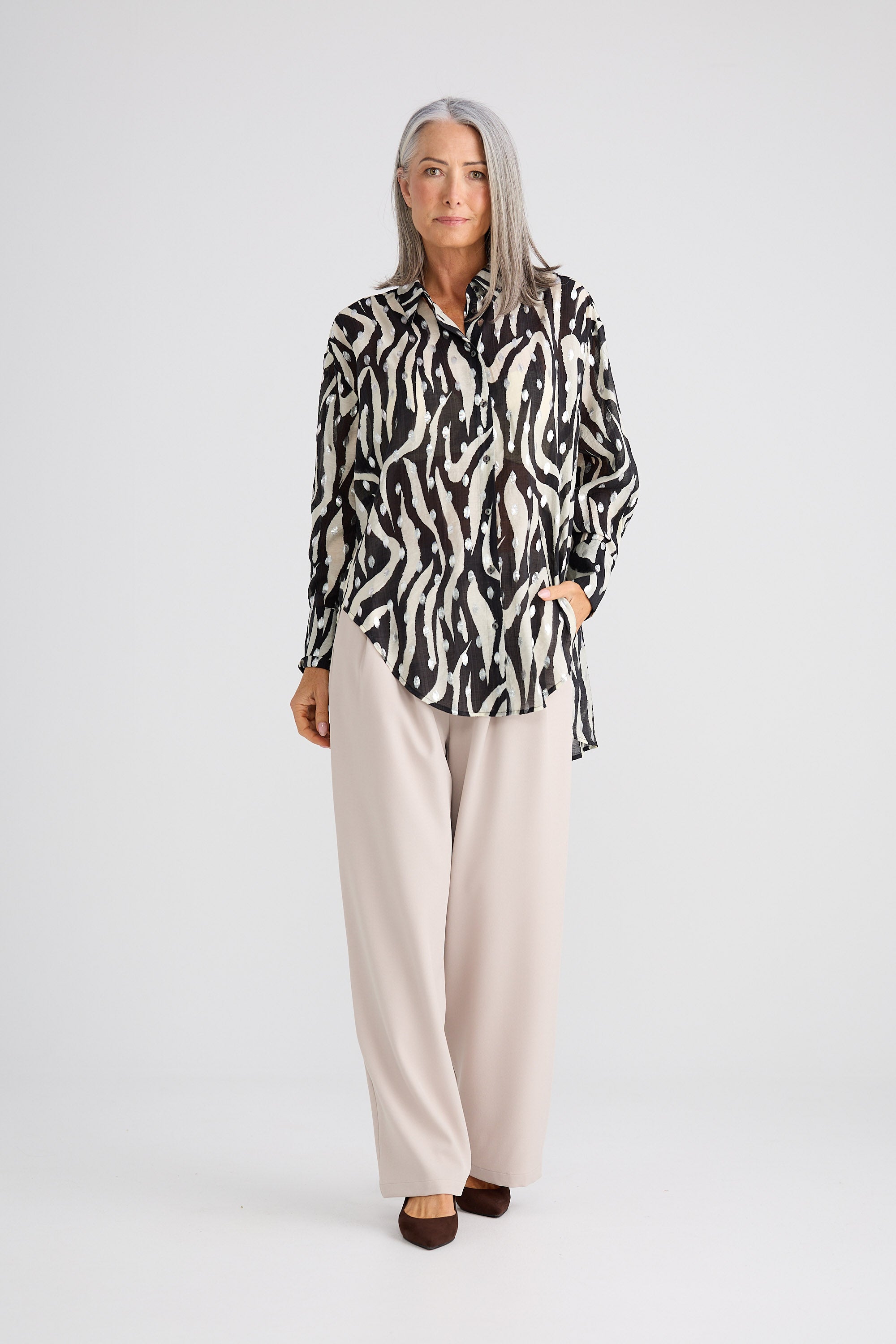 Woman wearing a patterned blouse and beige pants on a white background