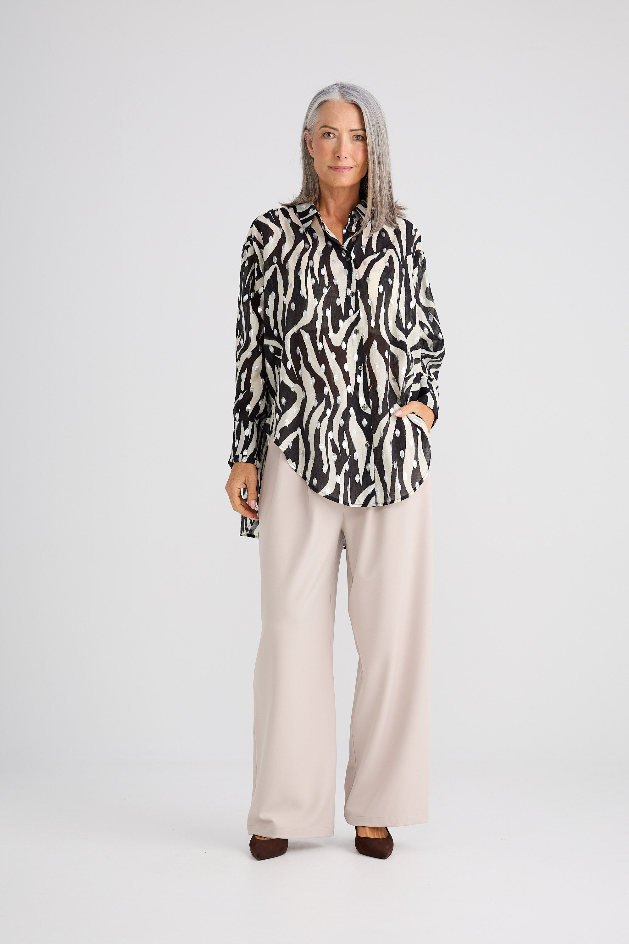 Woman wearing a patterned shirt and beige pants on a white background