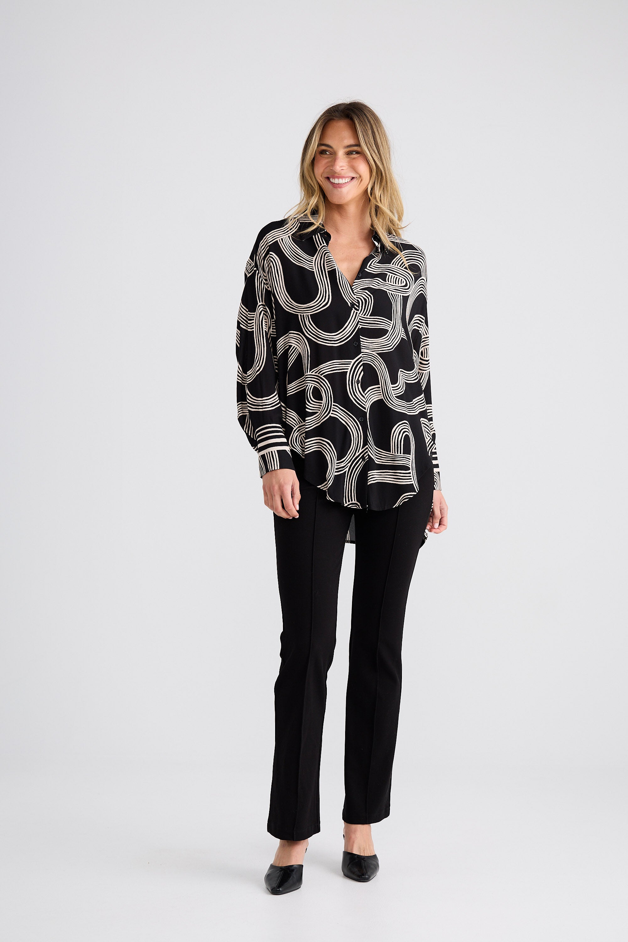 Woman wearing a black and white patterned blouse with black pants on a white background
