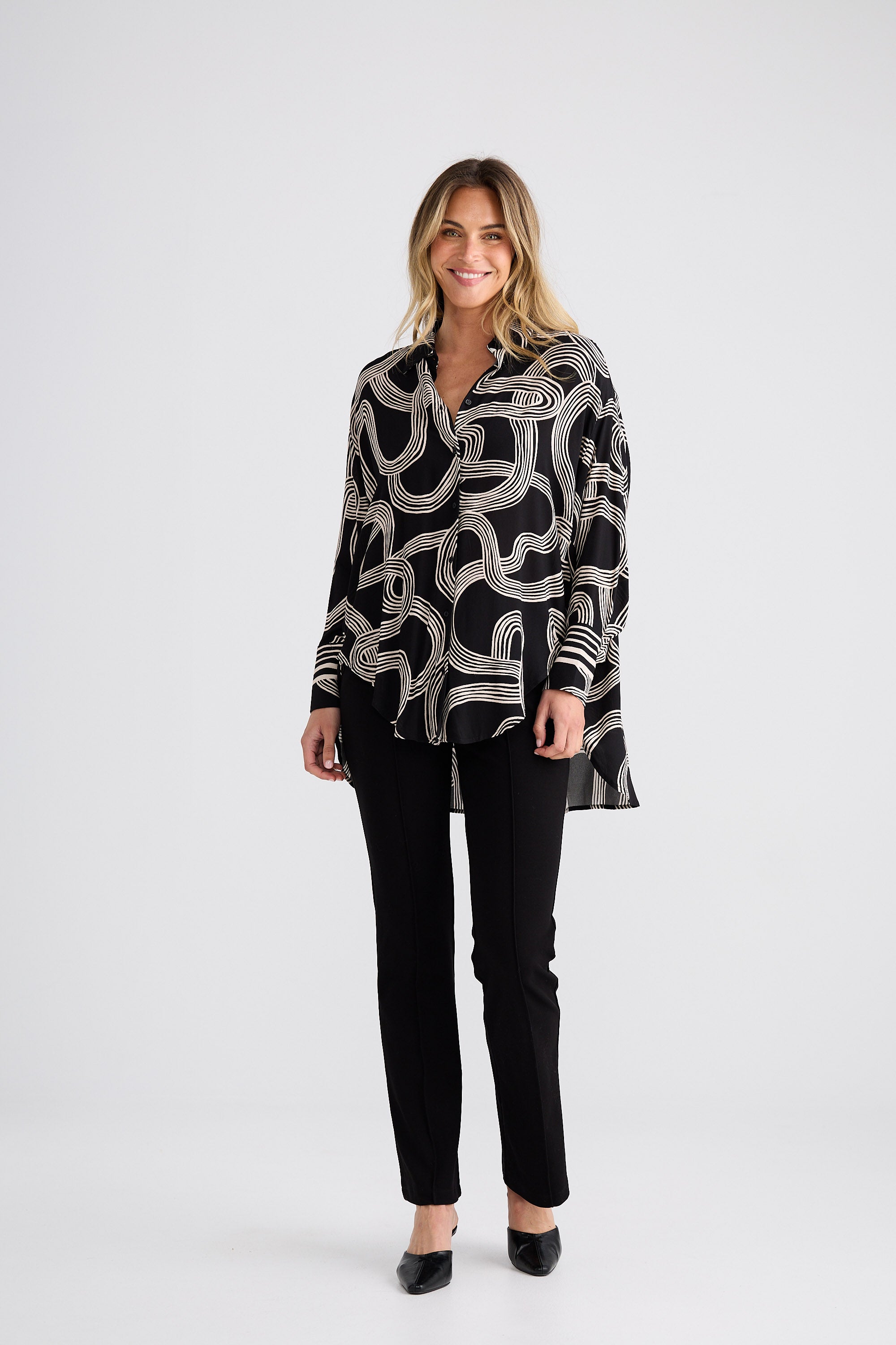 Woman wearing a black and white patterned shirt with black pants on a white background