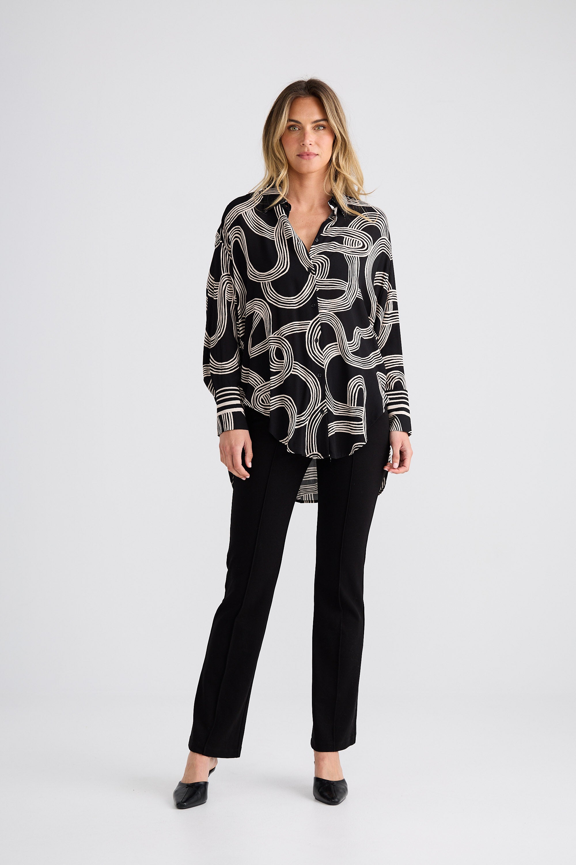 Woman wearing a black patterned shirt and black pants on a white background