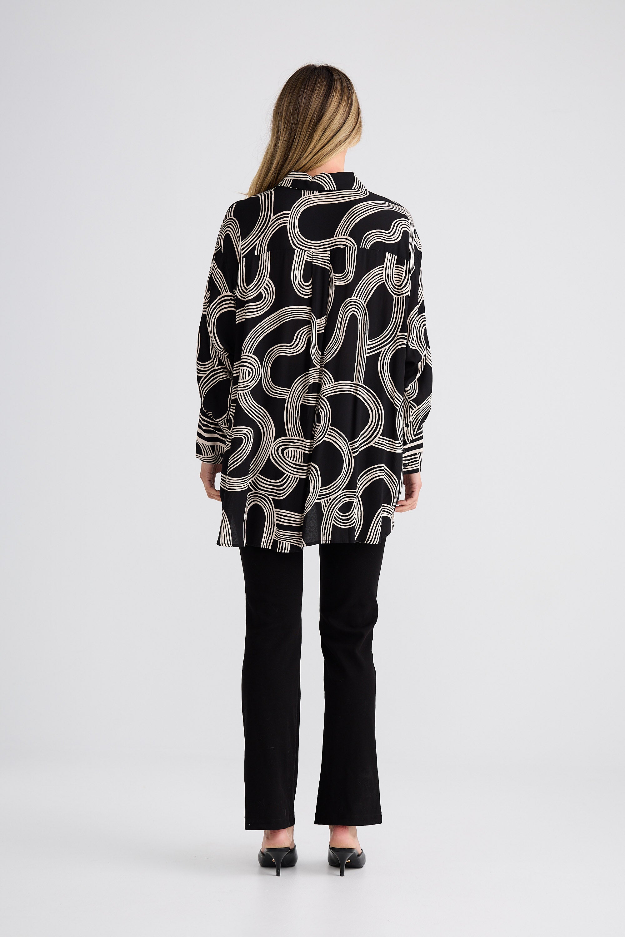 Person wearing a black and white patterned shirt with black pants on a white background