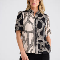 Woman wearing a black and white patterned blouse on a plain background