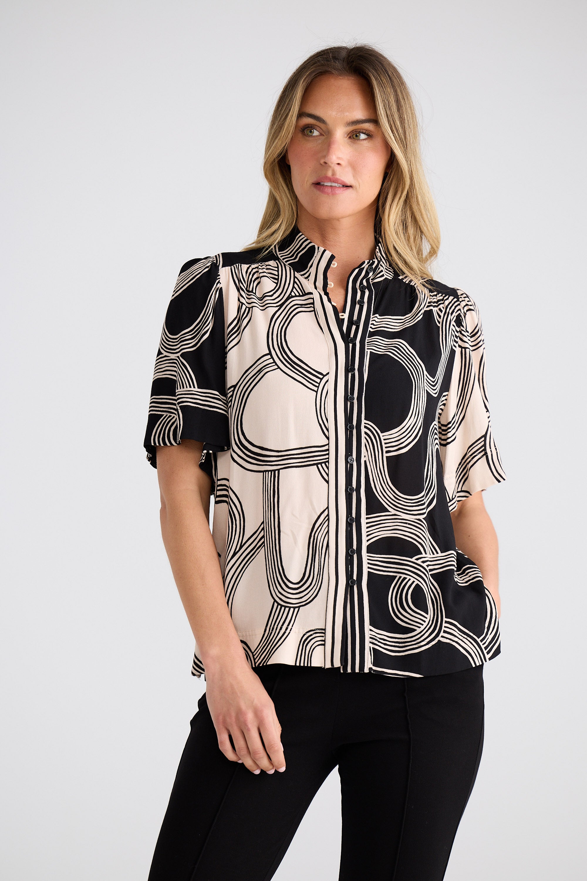 Woman wearing a black and white patterned blouse on a plain background