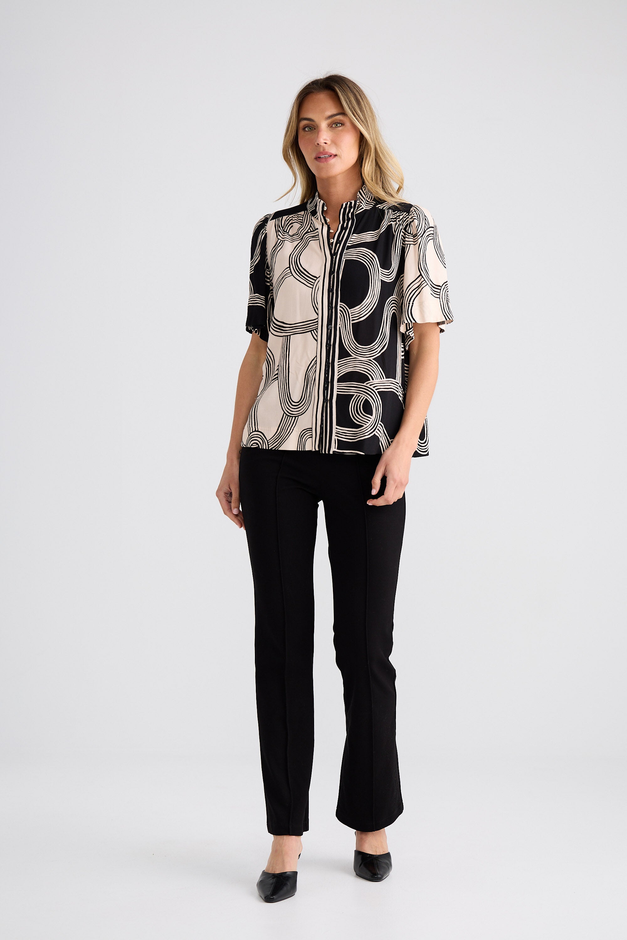 Woman wearing a patterned blouse and black pants on a white background
