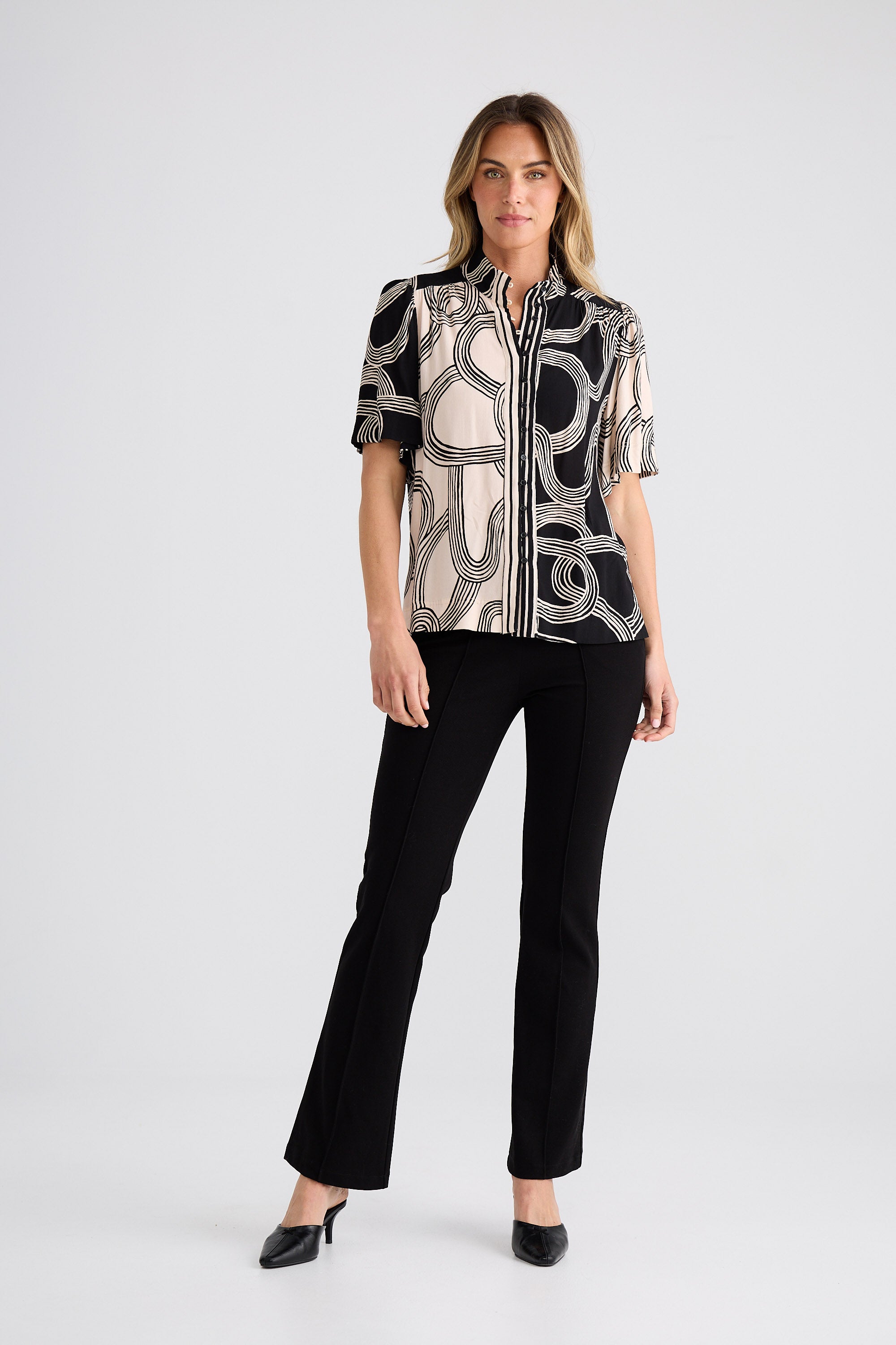 Woman wearing a patterned shirt and black pants on a white background