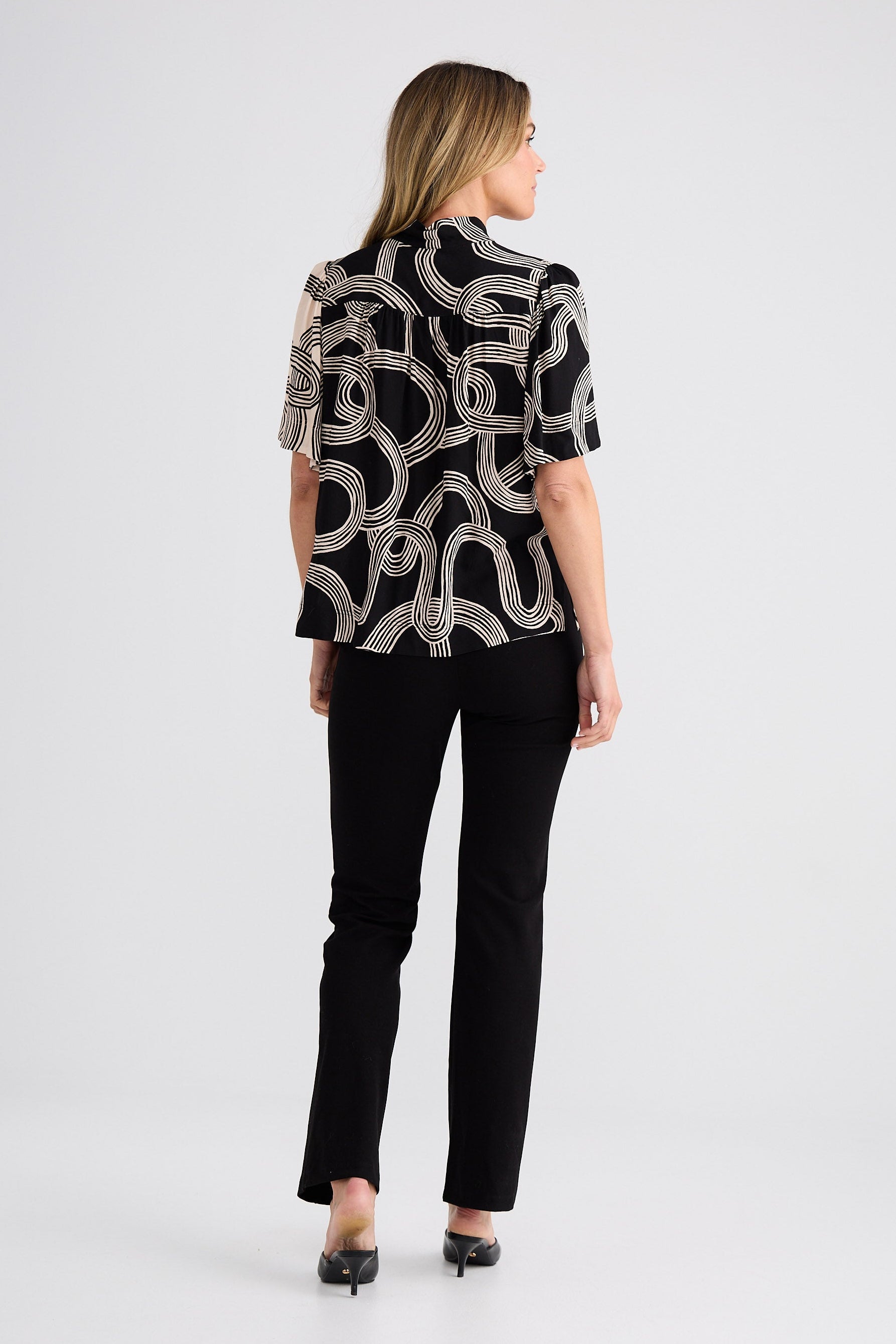 Woman wearing a black and white patterned blouse with black pants on a white background