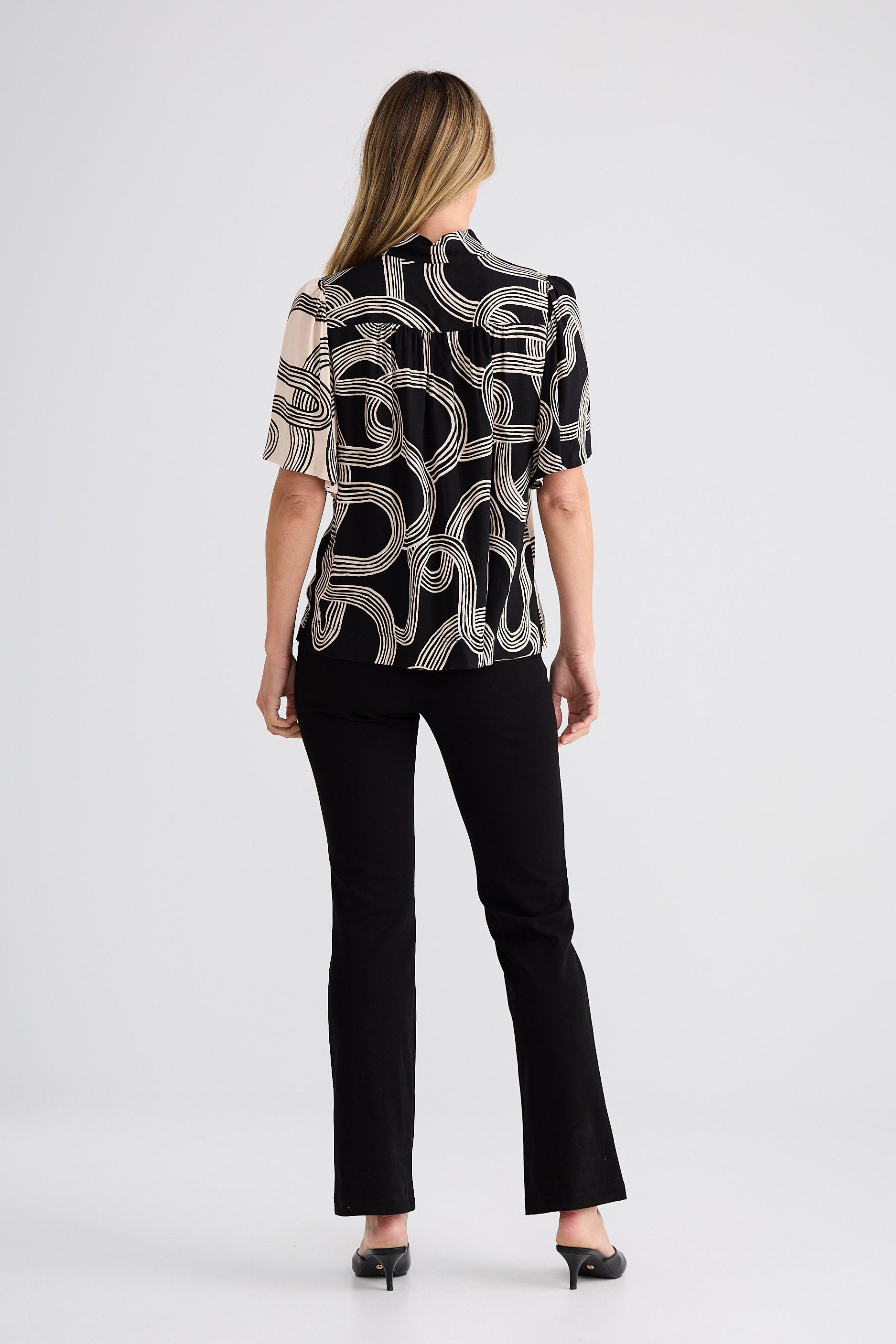 Woman wearing a patterned blouse and black pants on a white background