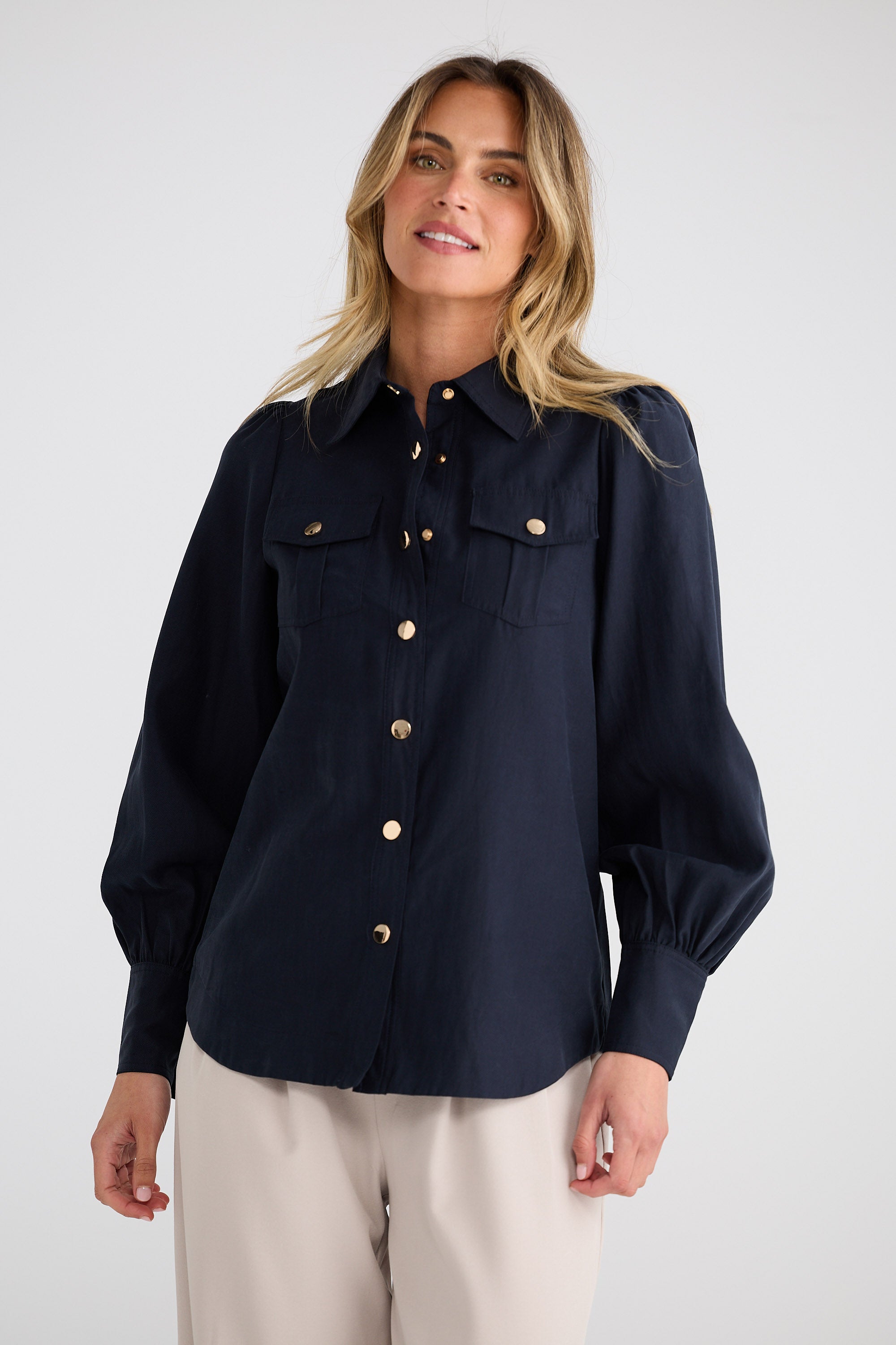 Woman wearing a navy blue blouse with gold buttons on a white background