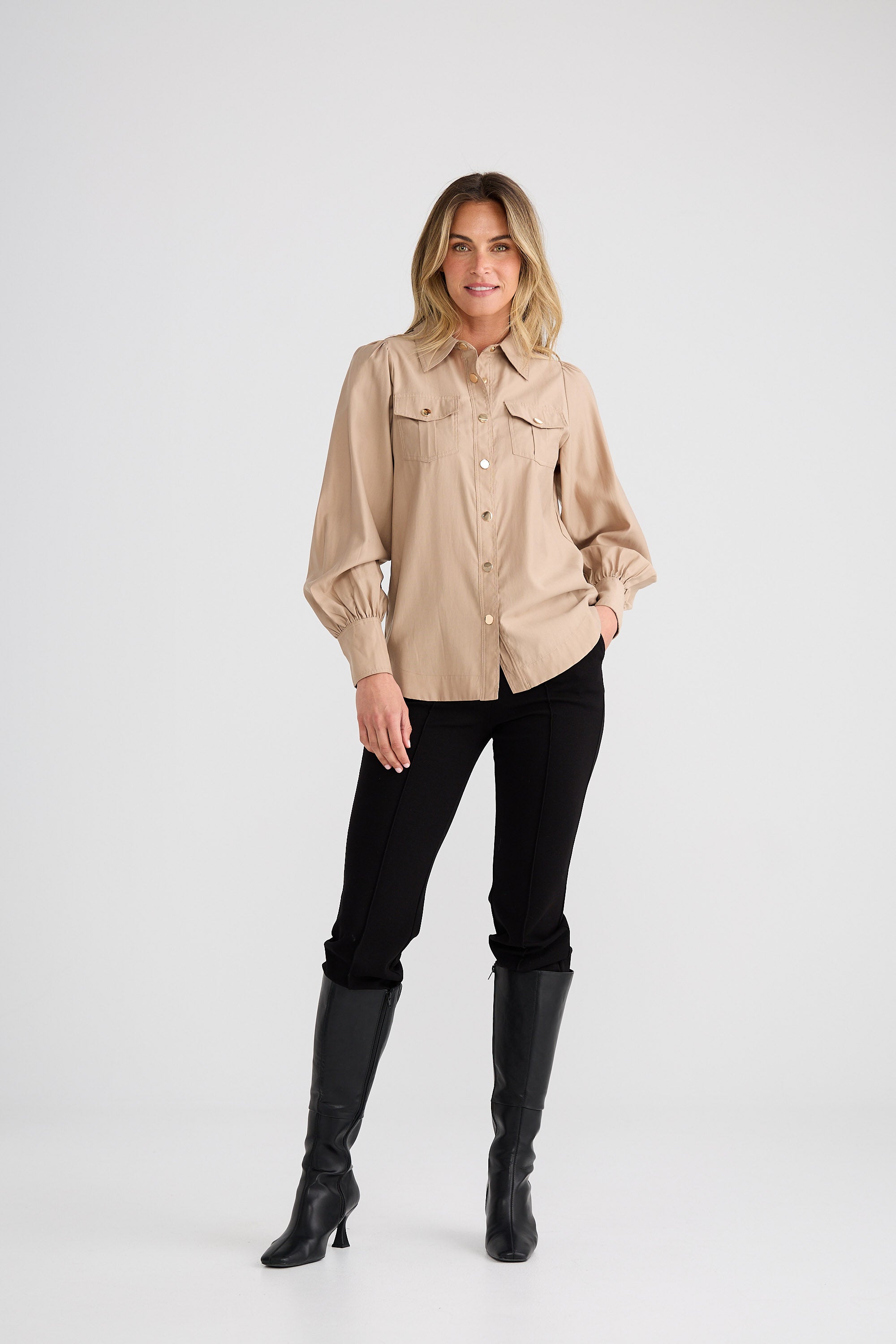 Woman wearing a beige shirt, black pants, and black boots on a white background