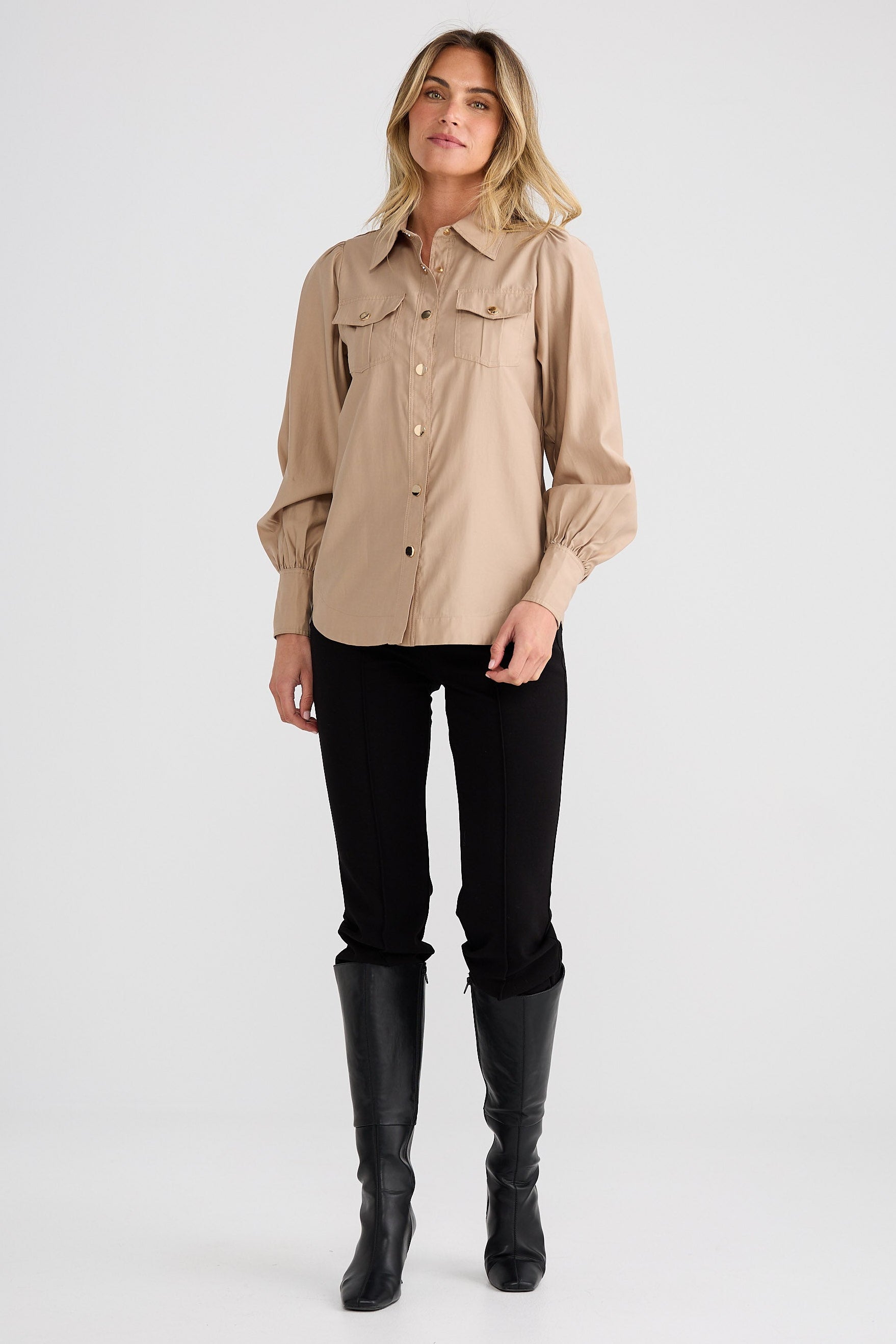 Woman wearing a beige shirt, black pants, and black boots on a white background