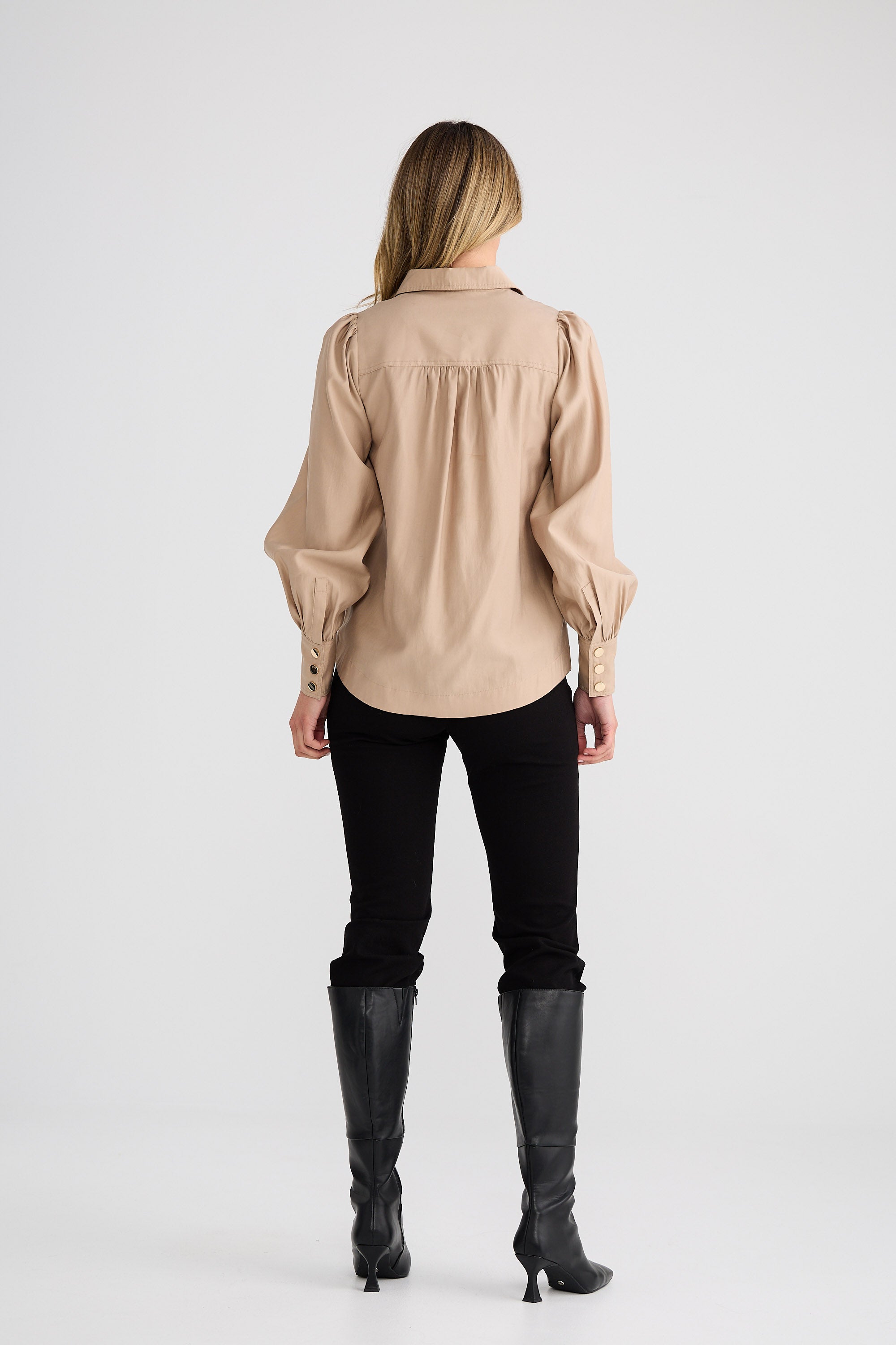 Person wearing a beige blouse, black pants, and black boots on a white background
