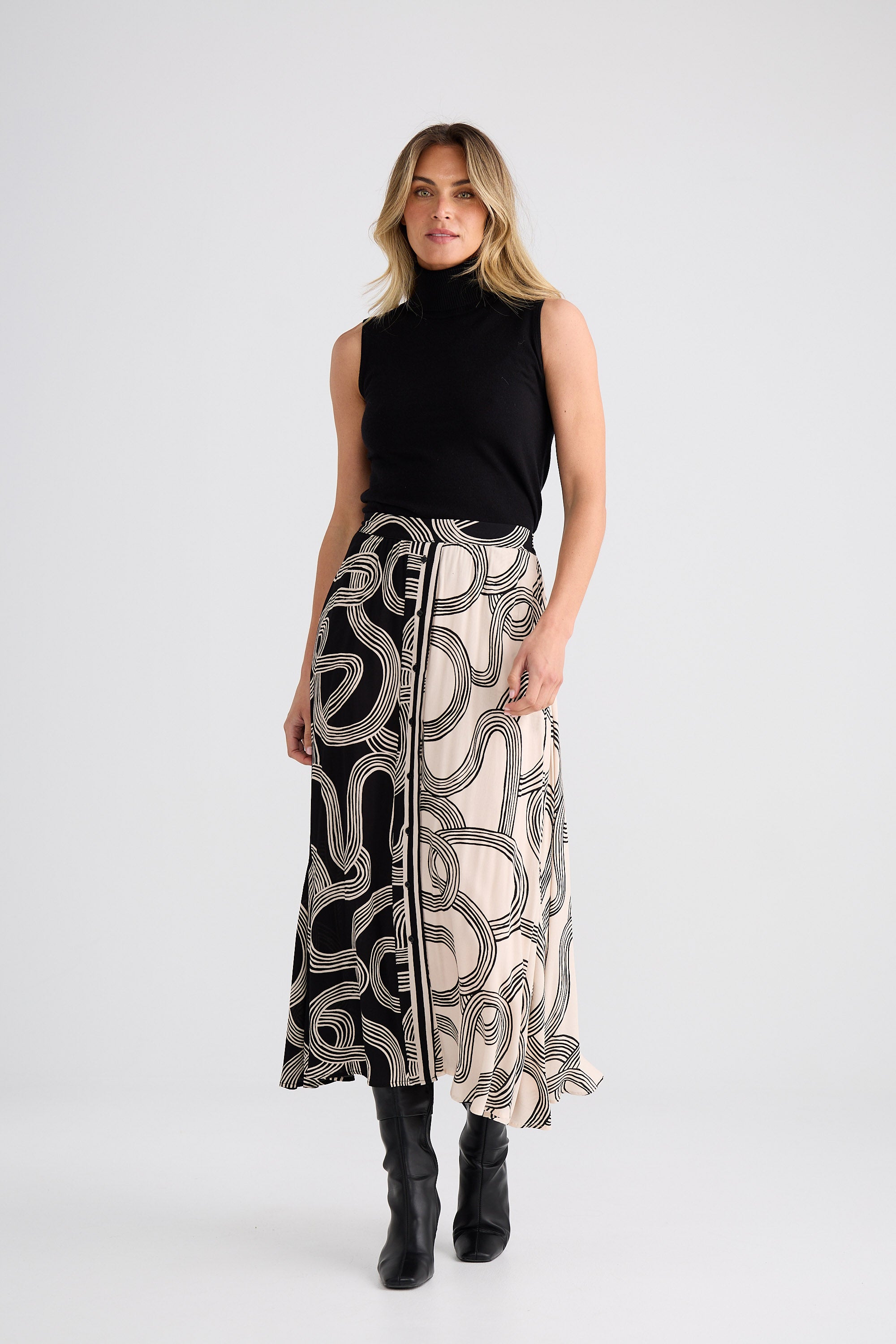 Woman wearing a black sleeveless top and patterned skirt on a white background