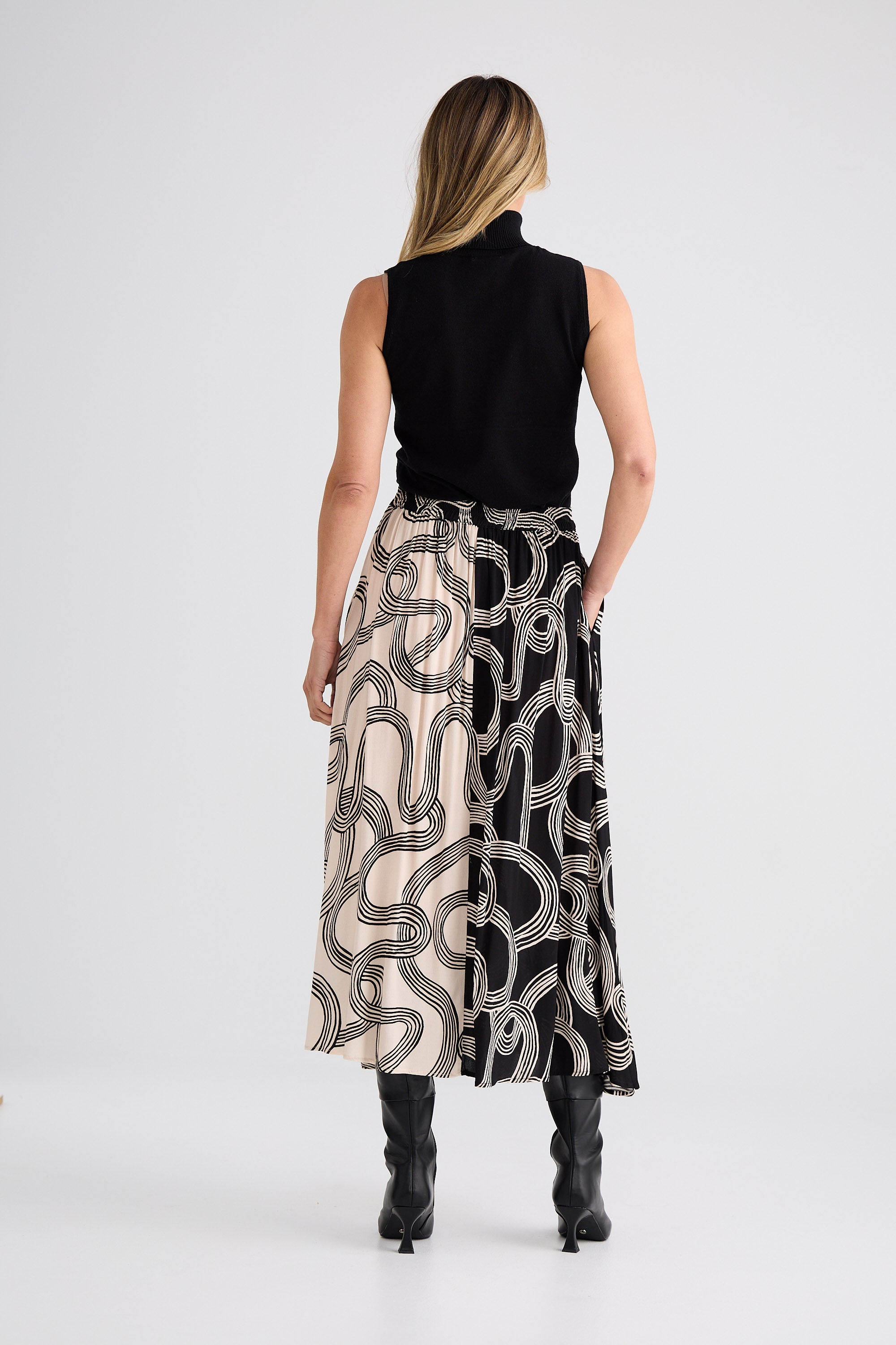 Woman wearing a black sleeveless top and patterned skirt on a white background