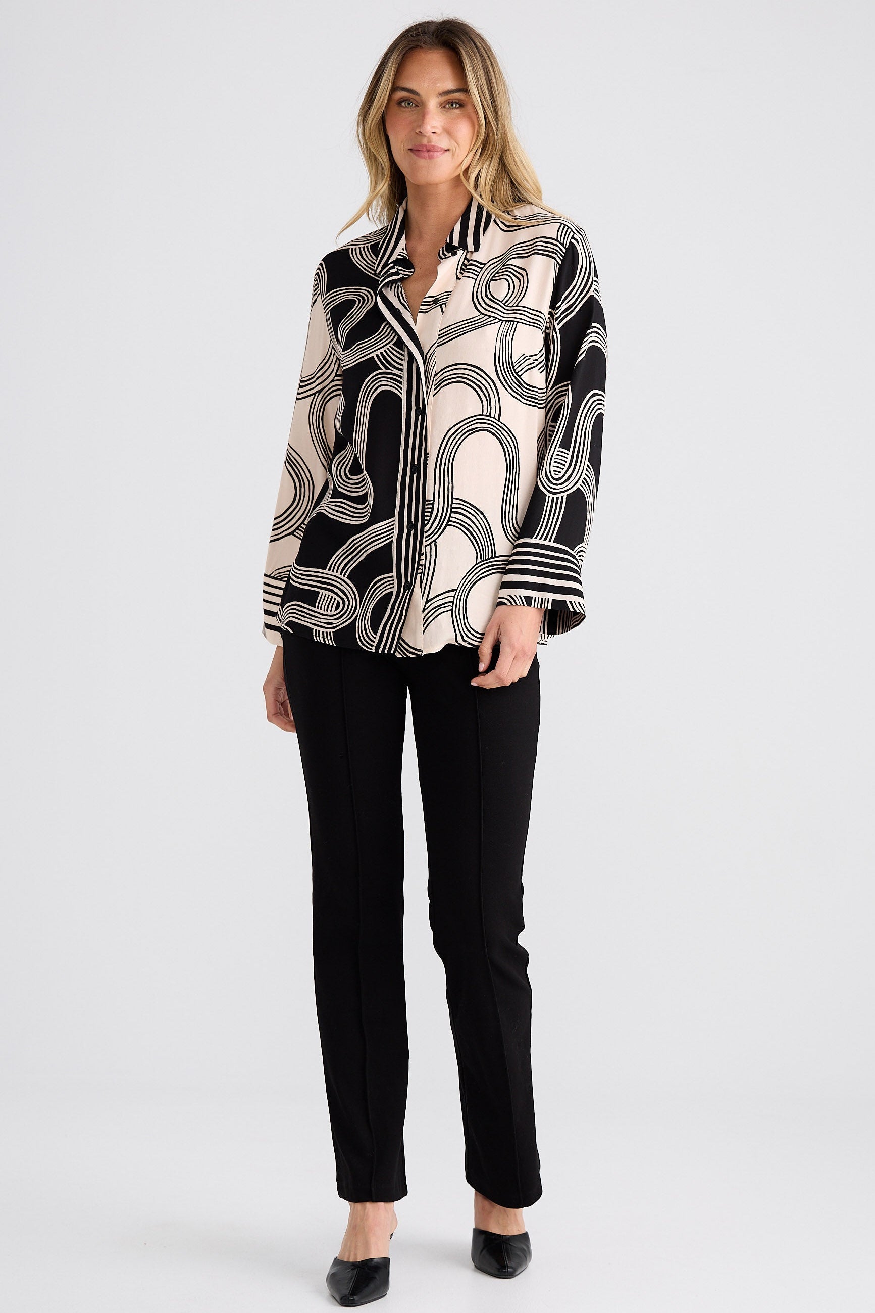 Woman wearing a black and white patterned blouse with black pants on a white background