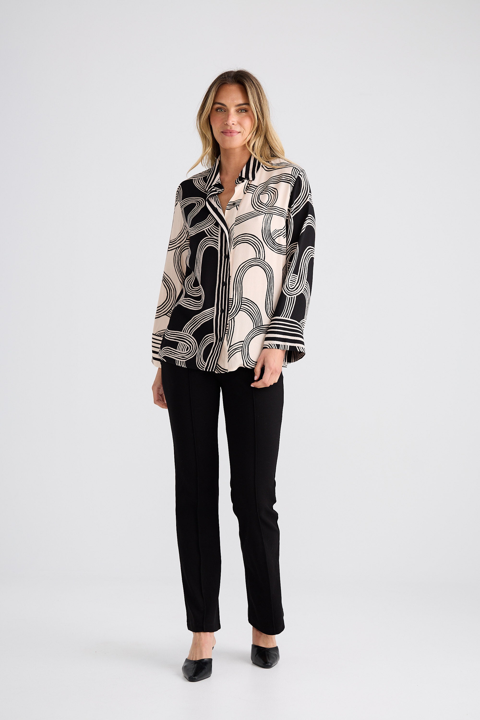 Woman wearing a black and white patterned blouse with black pants on a white background