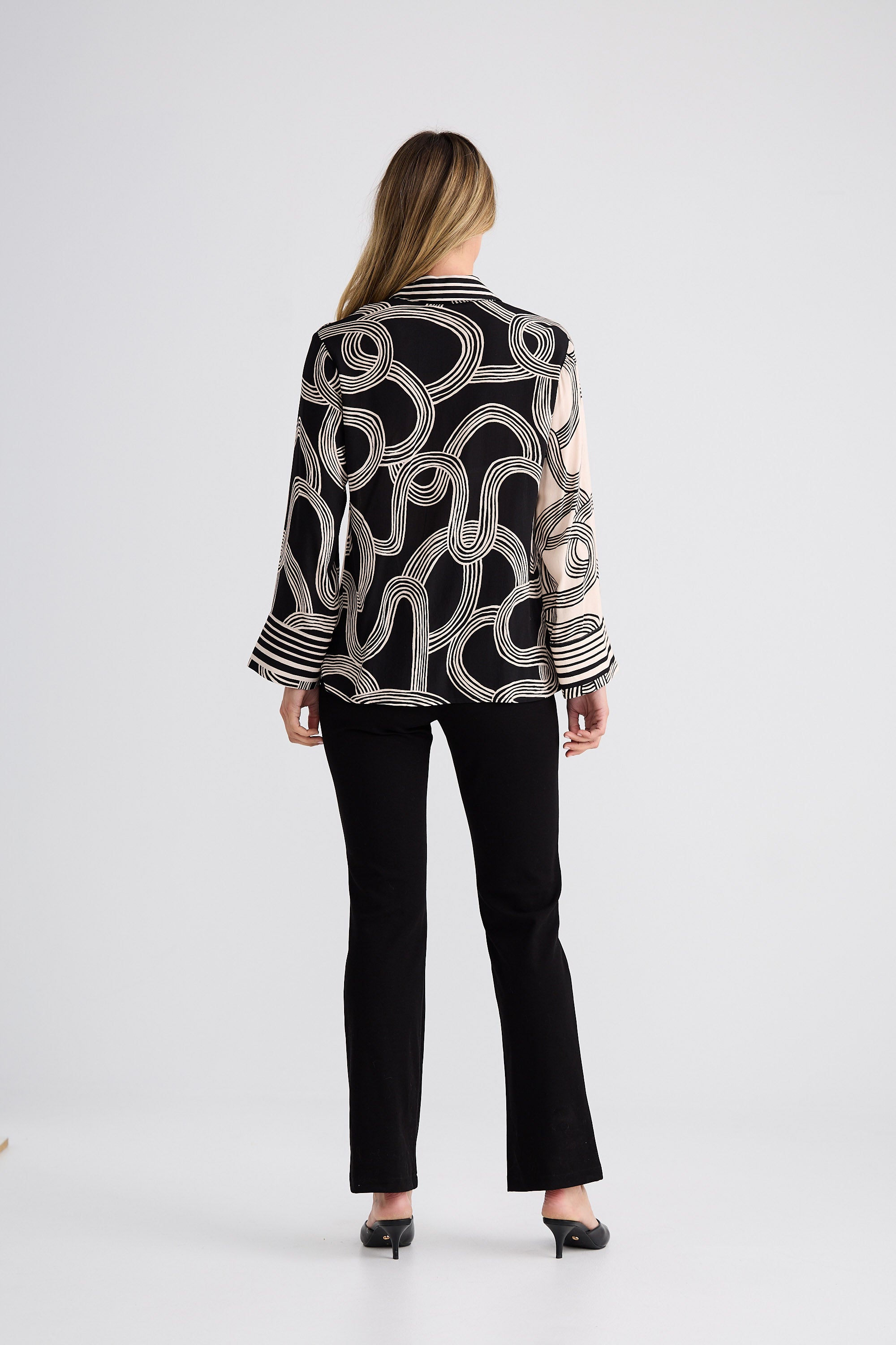 Woman wearing a black and white patterned blouse with black pants on a white background