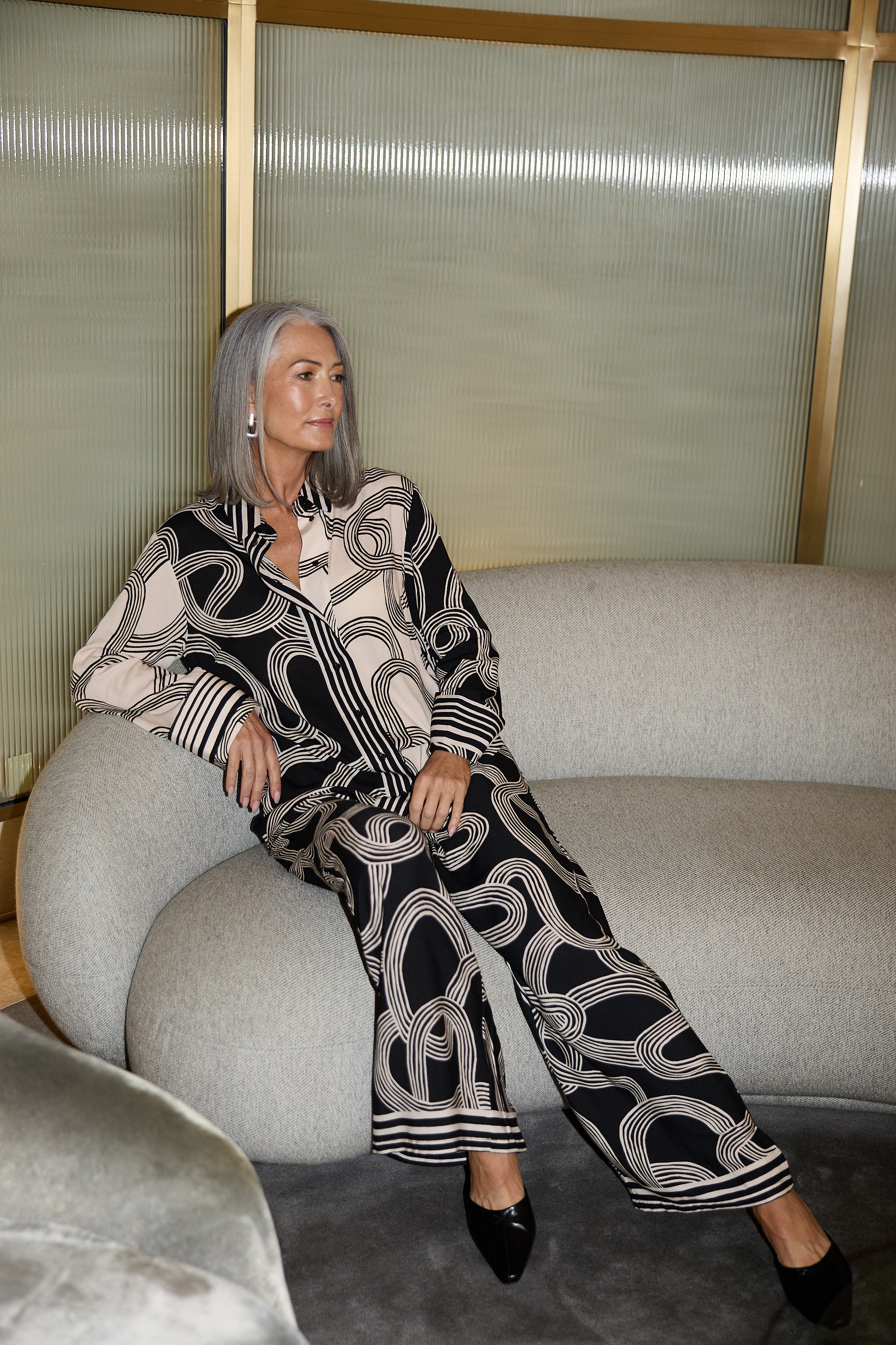 Woman in a black and white patterned outfit sitting on a gray sofa.