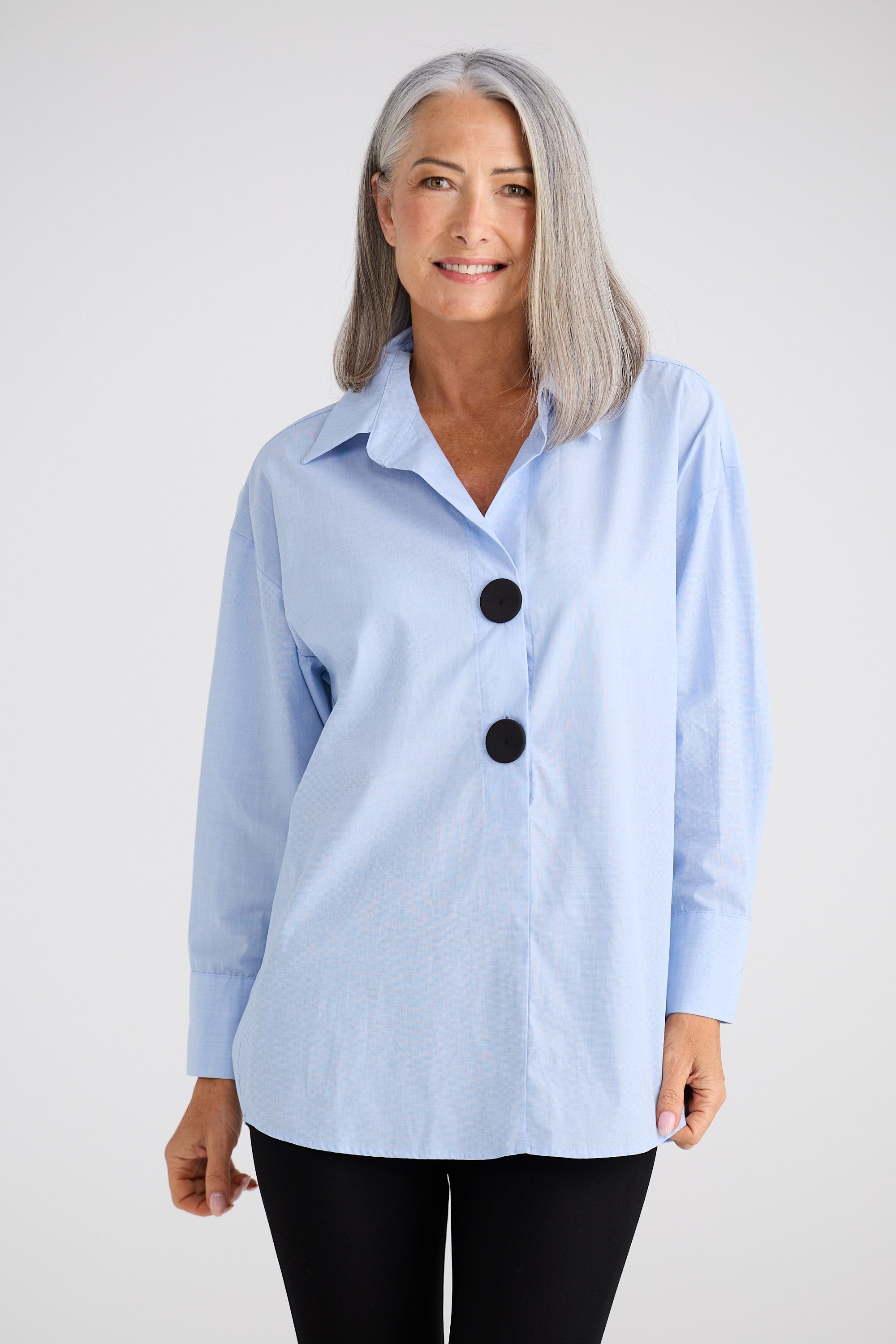 Woman wearing a light blue button-up shirt with black buttons on a white background