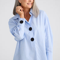 Woman wearing a light blue jacket with black buttons on a white background