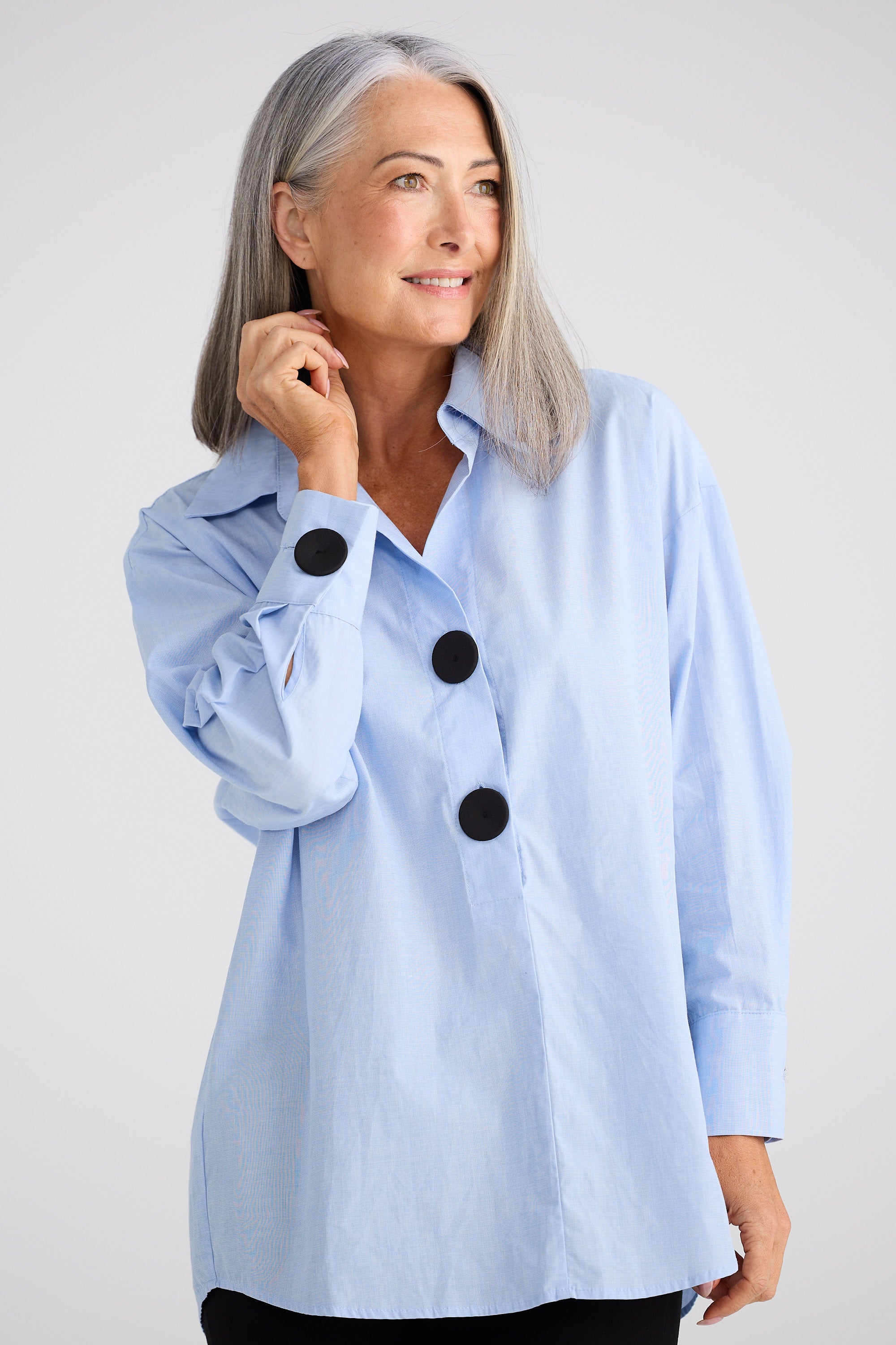 Woman wearing a light blue jacket with black buttons on a white background