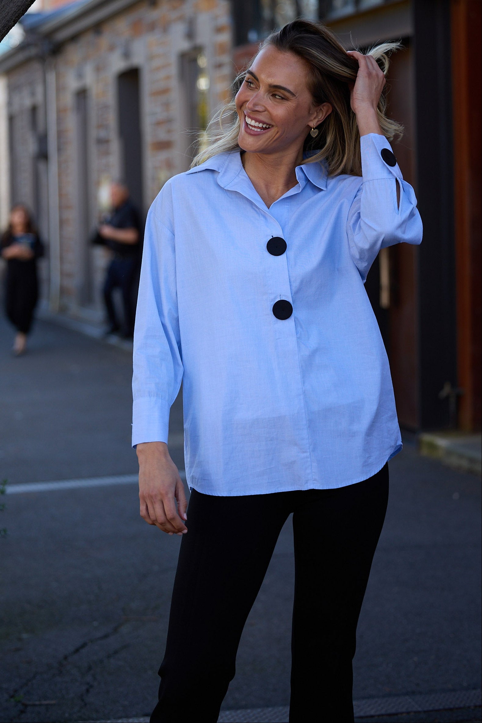 Woman in a light blue shirt with black buttons walking down a street.
