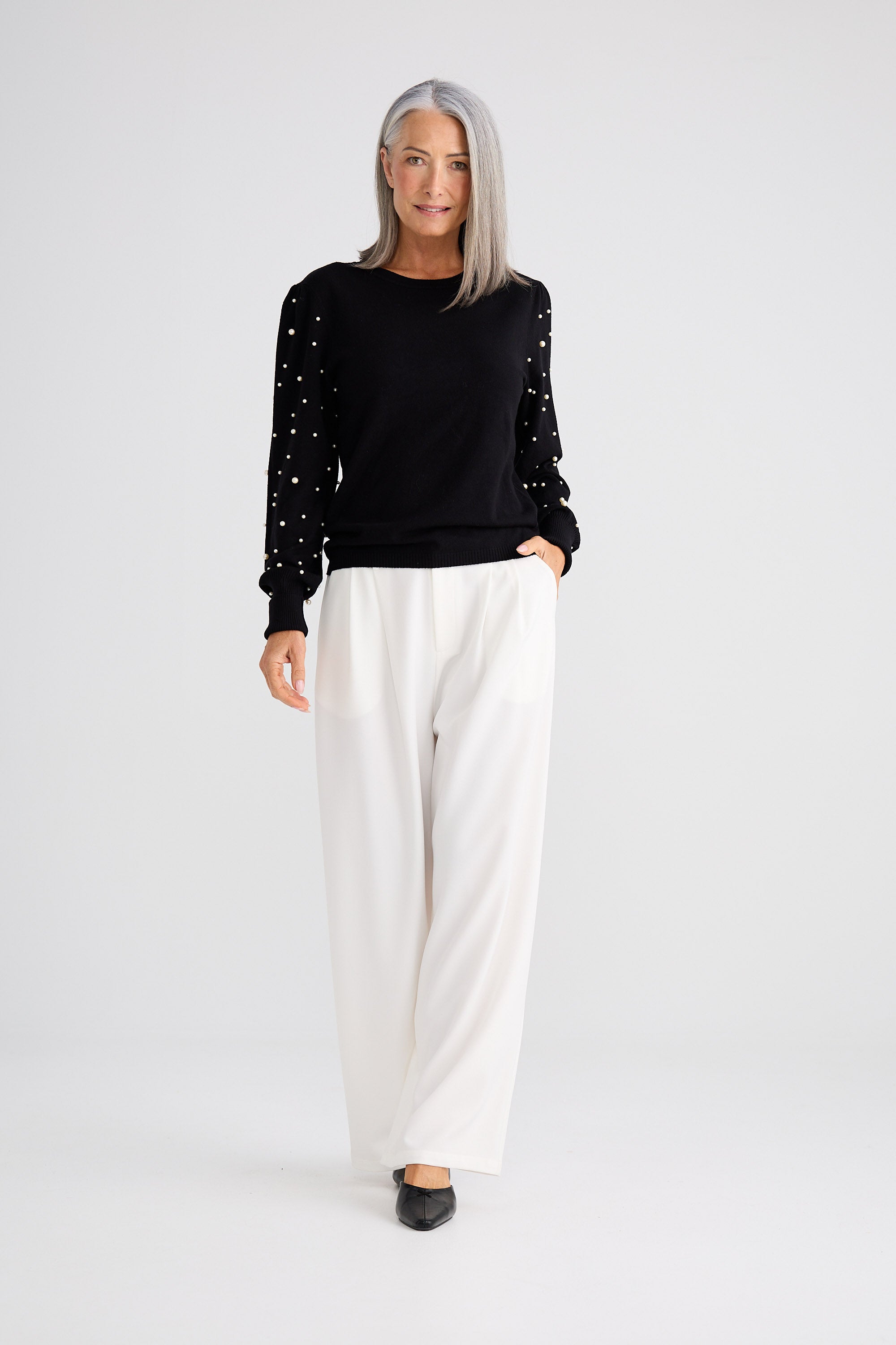 Woman wearing a black sweater with white polka dots and white pants on a white background