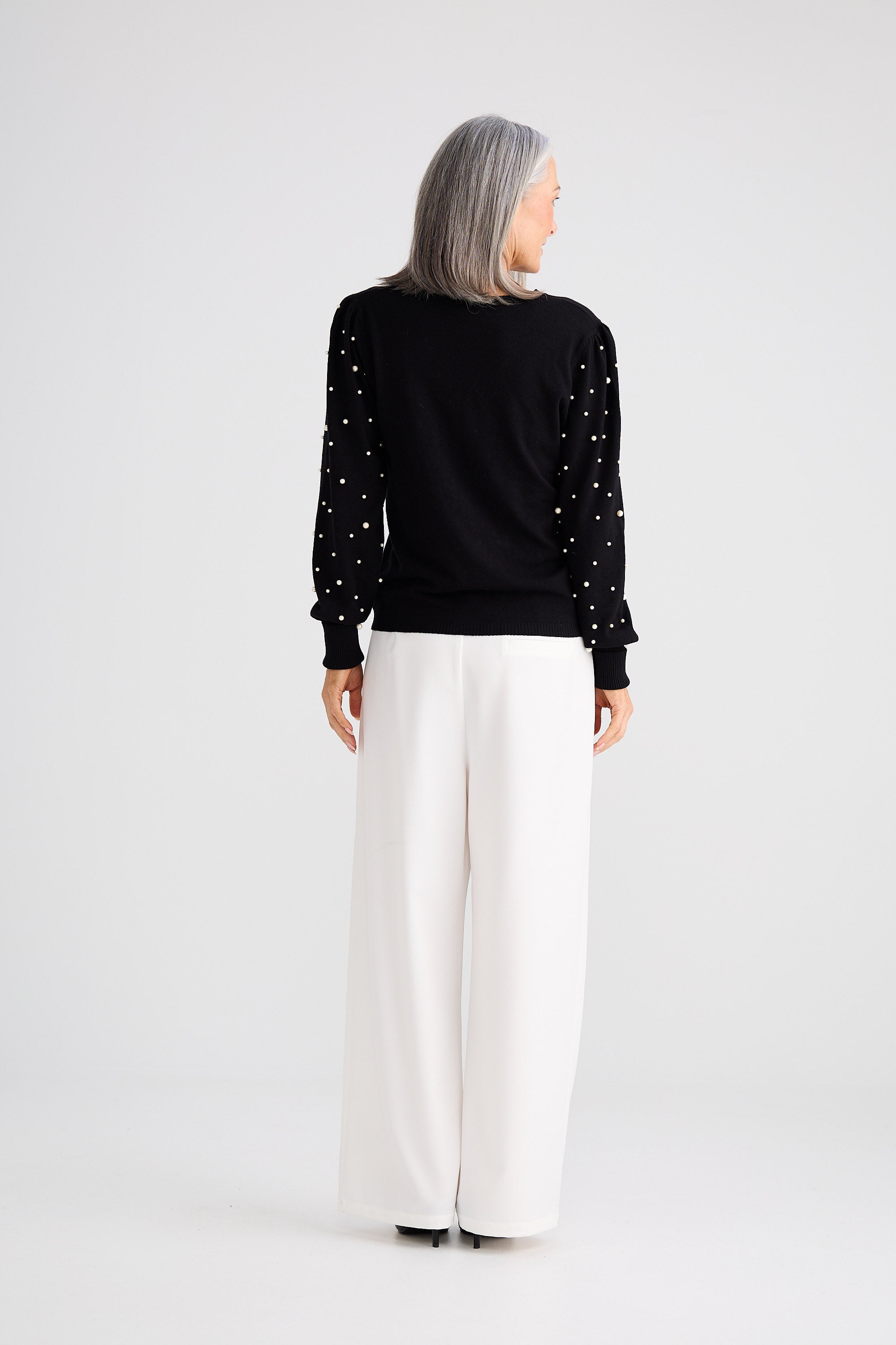 Person wearing a black sweater with white polka dots and white pants on a light gray background