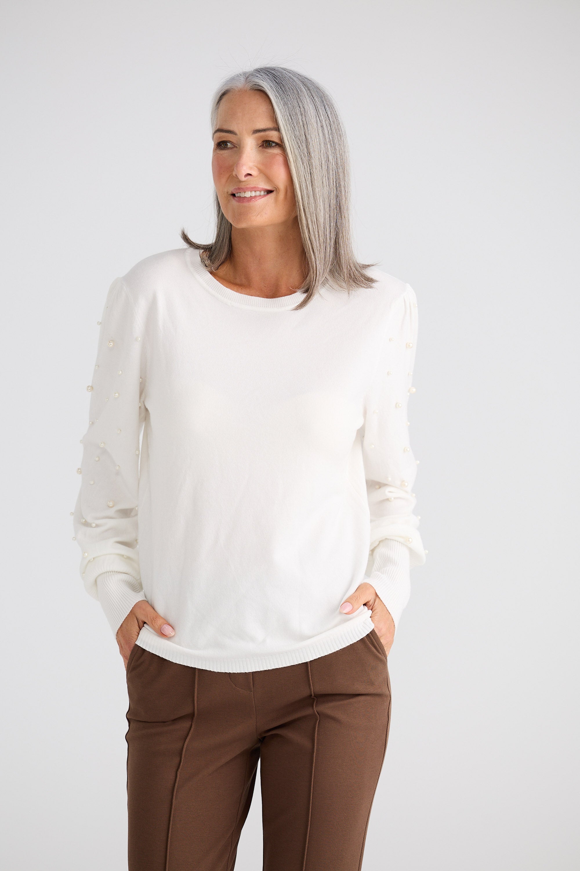 Woman wearing a white sweater and brown pants on a plain background