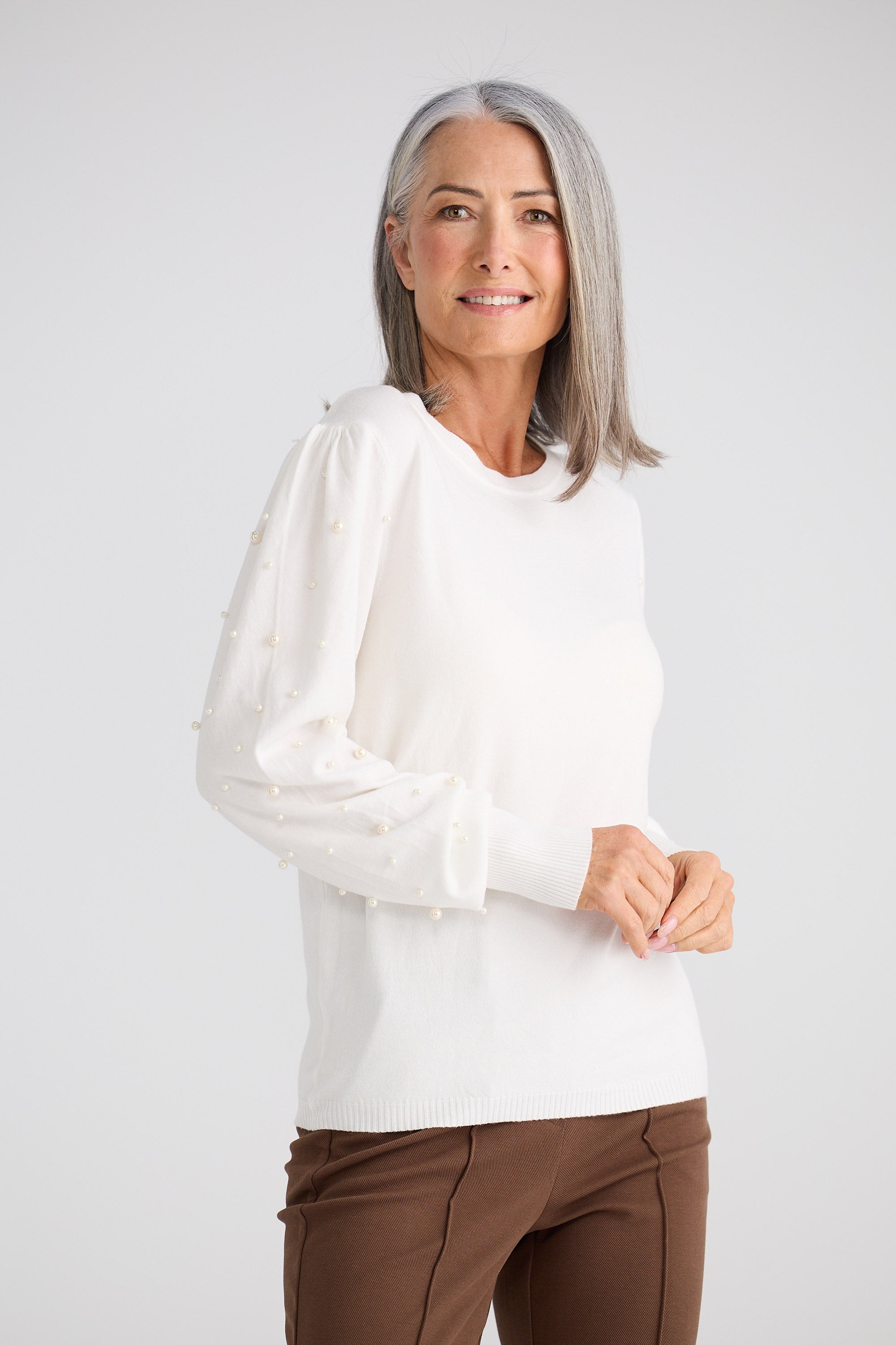 Woman wearing a white blouse and brown pants on a plain background