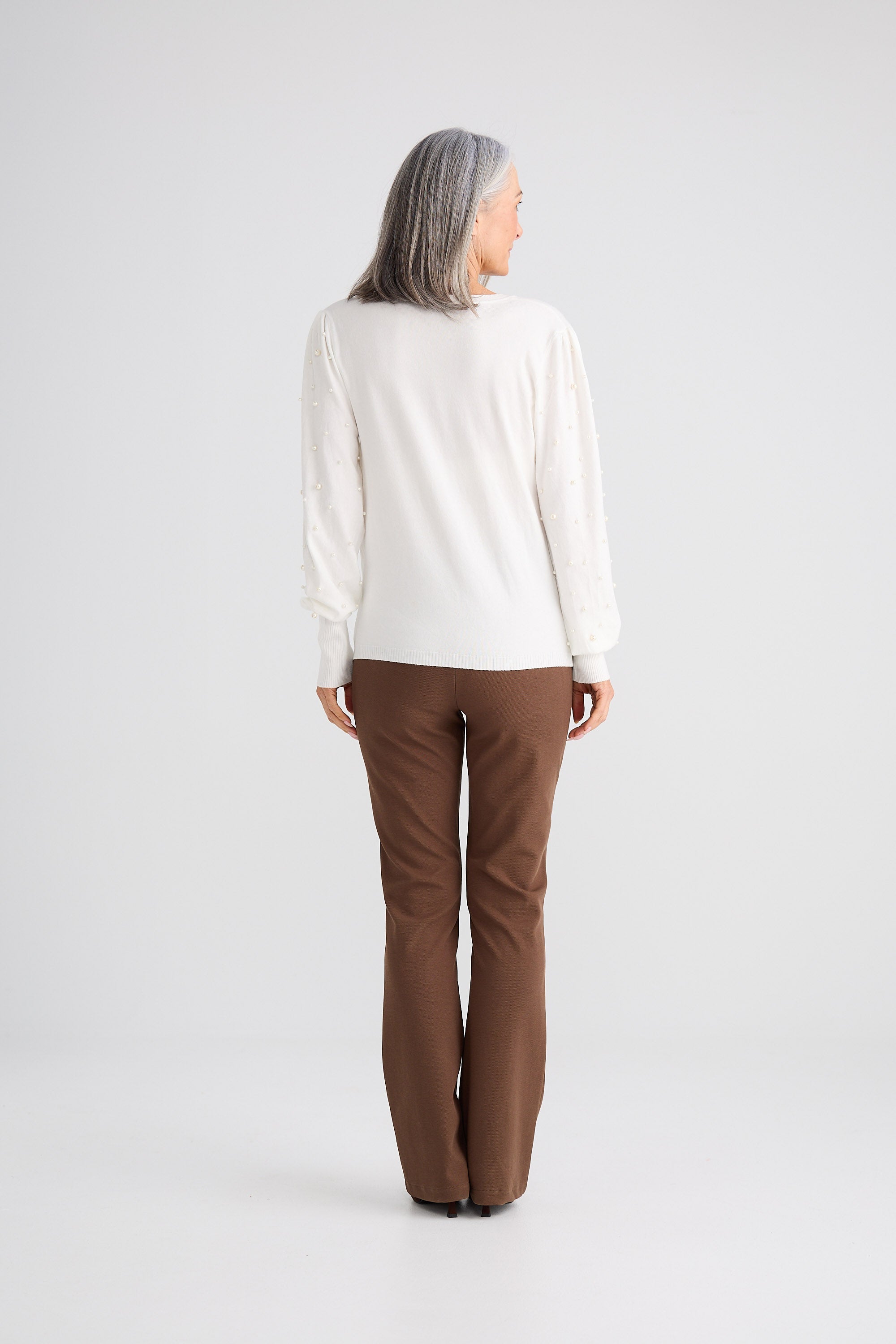 Person wearing a white sweater and brown pants on a white background