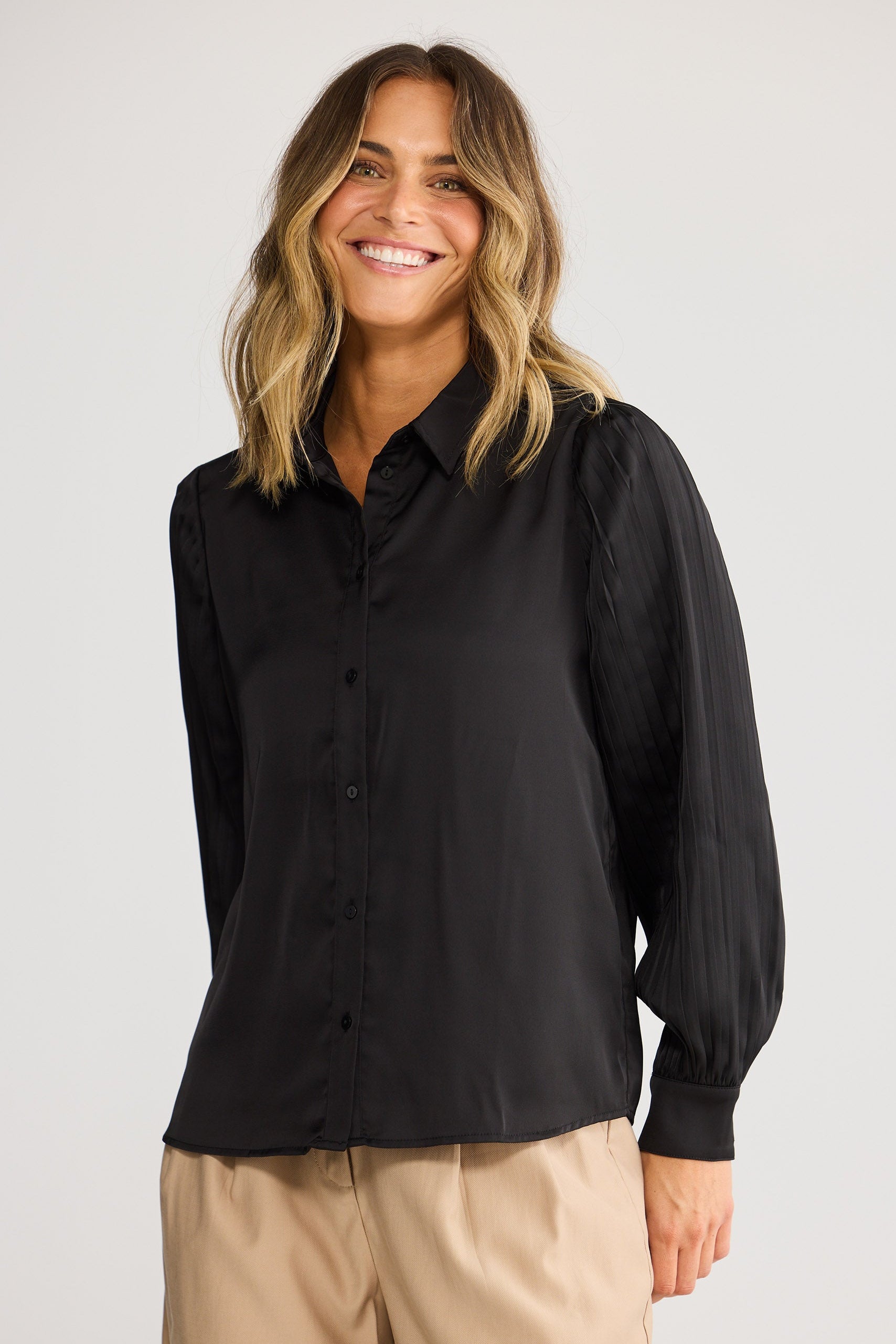 Woman wearing a black shirt and beige pants against a white background